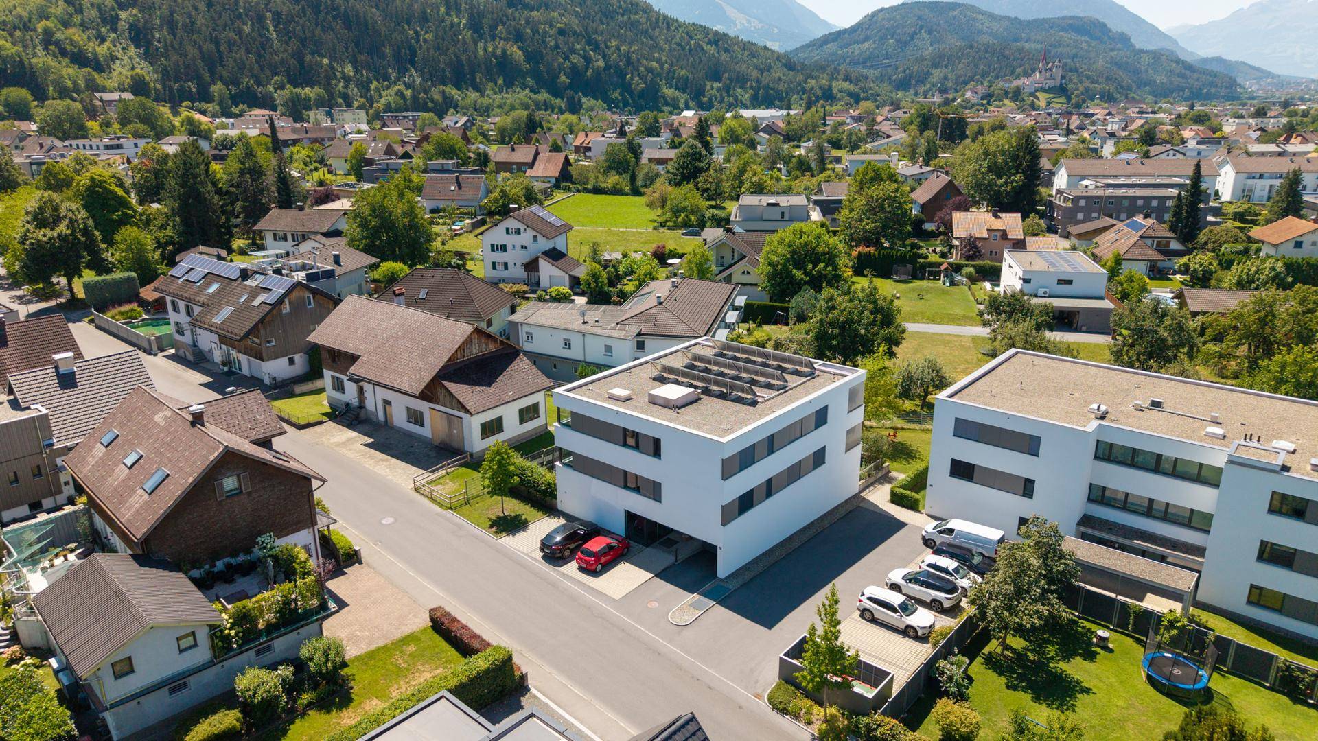 Luftaufnahme einer modernen Wohnanlage in einer grünen Umgebung mit Bergblick und Photovoltaikanlage.