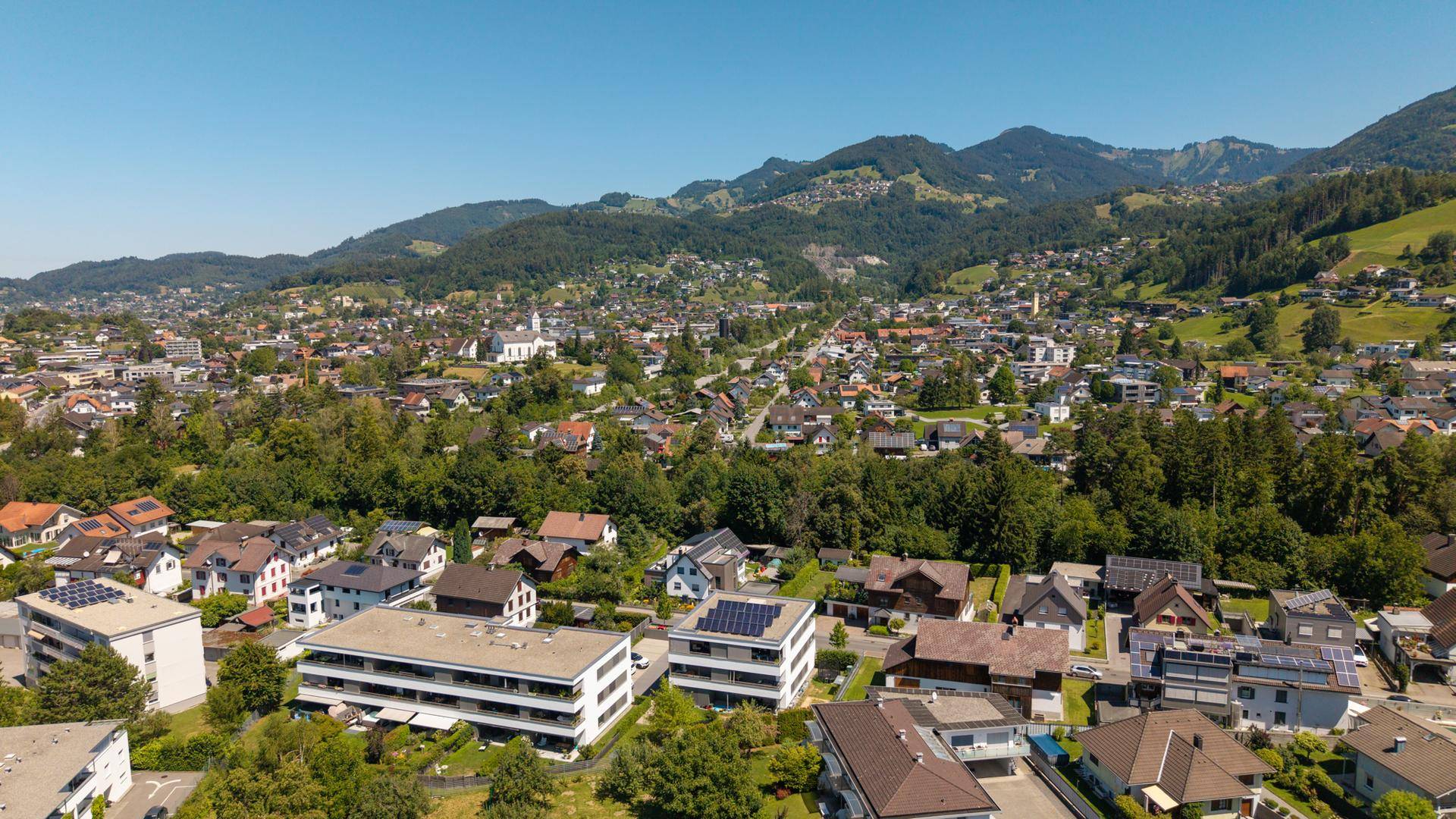 Weitläufige Luftaufnahme einer Wohngegend mit Gebäuden und grünen Hügeln.