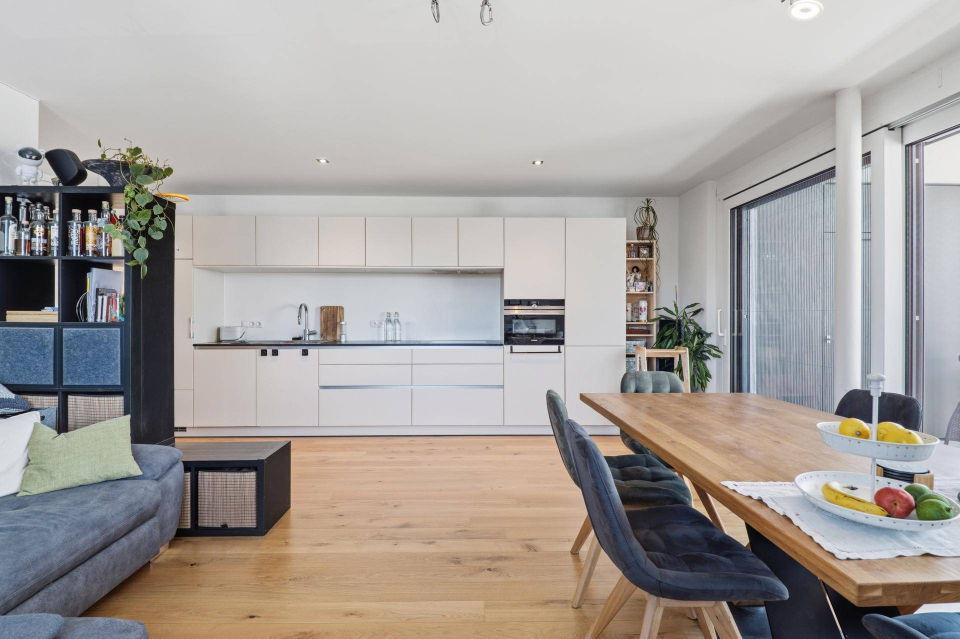 Offener Wohnbereich mit moderner Einbauküche, Esstisch und Zugang zum Balkon.