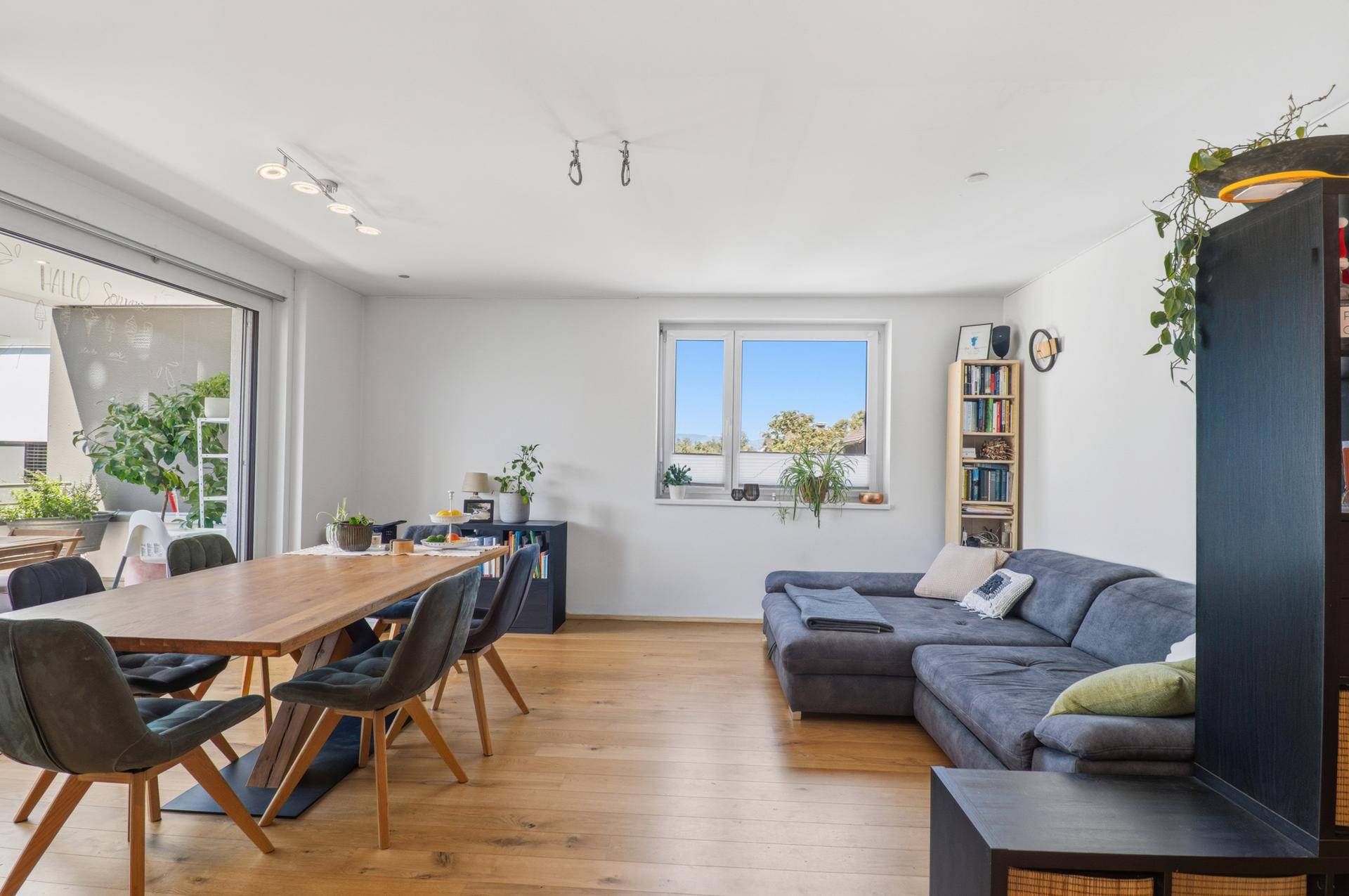 Heller Wohn- und Essbereich mit Holzboden, Sofa und Esstisch, sowie Fensterblick.
