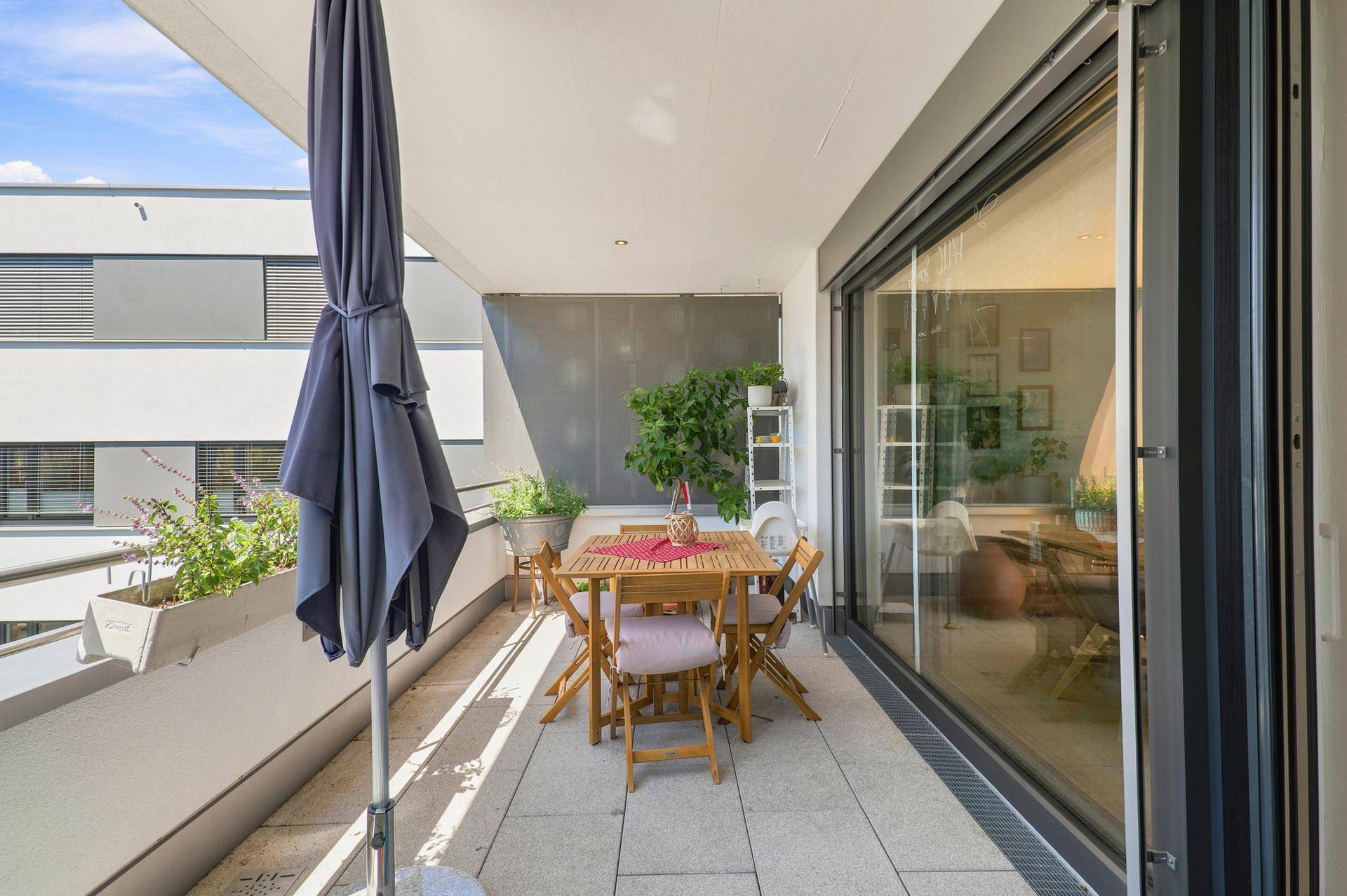 Heller Balkon mit Esstisch, Sonnenschirm und Blick auf die Umgebung.