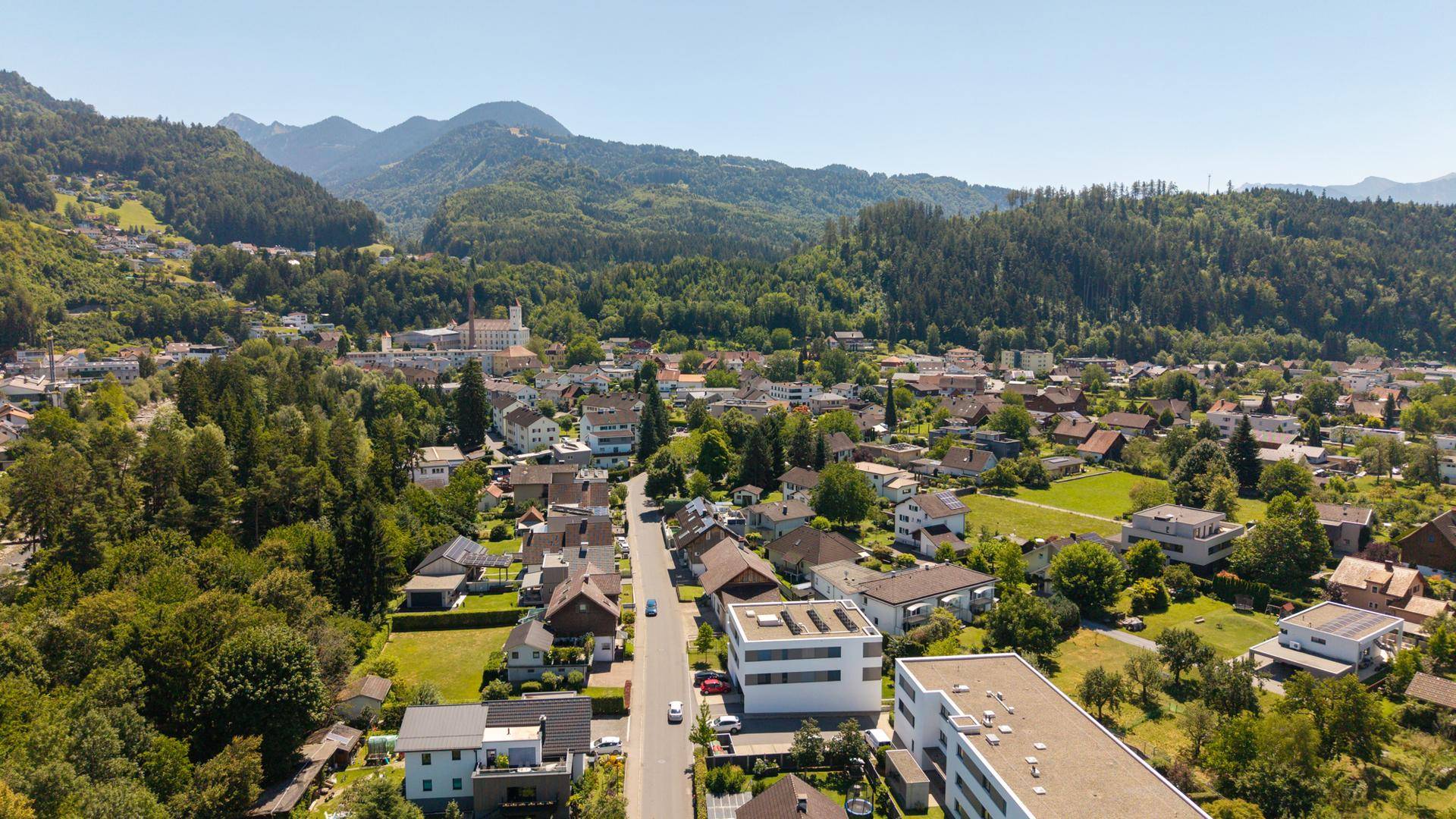 Luftaufnahme einer Wohnsiedlung mit viel Grün und Bergen im Hintergrund.