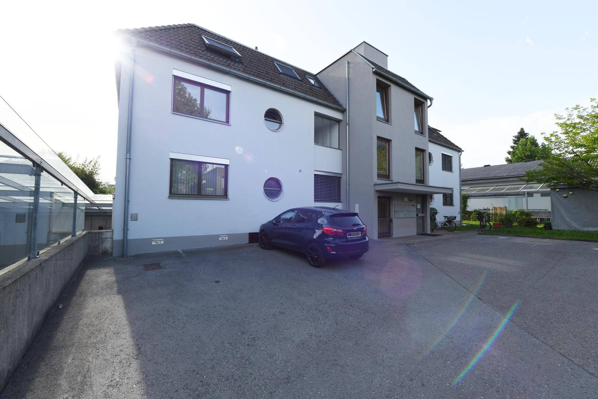 Modernes Mehrfamilienhaus mit Parkplätzen und gepflegter Fassade unter blauem Himmel.