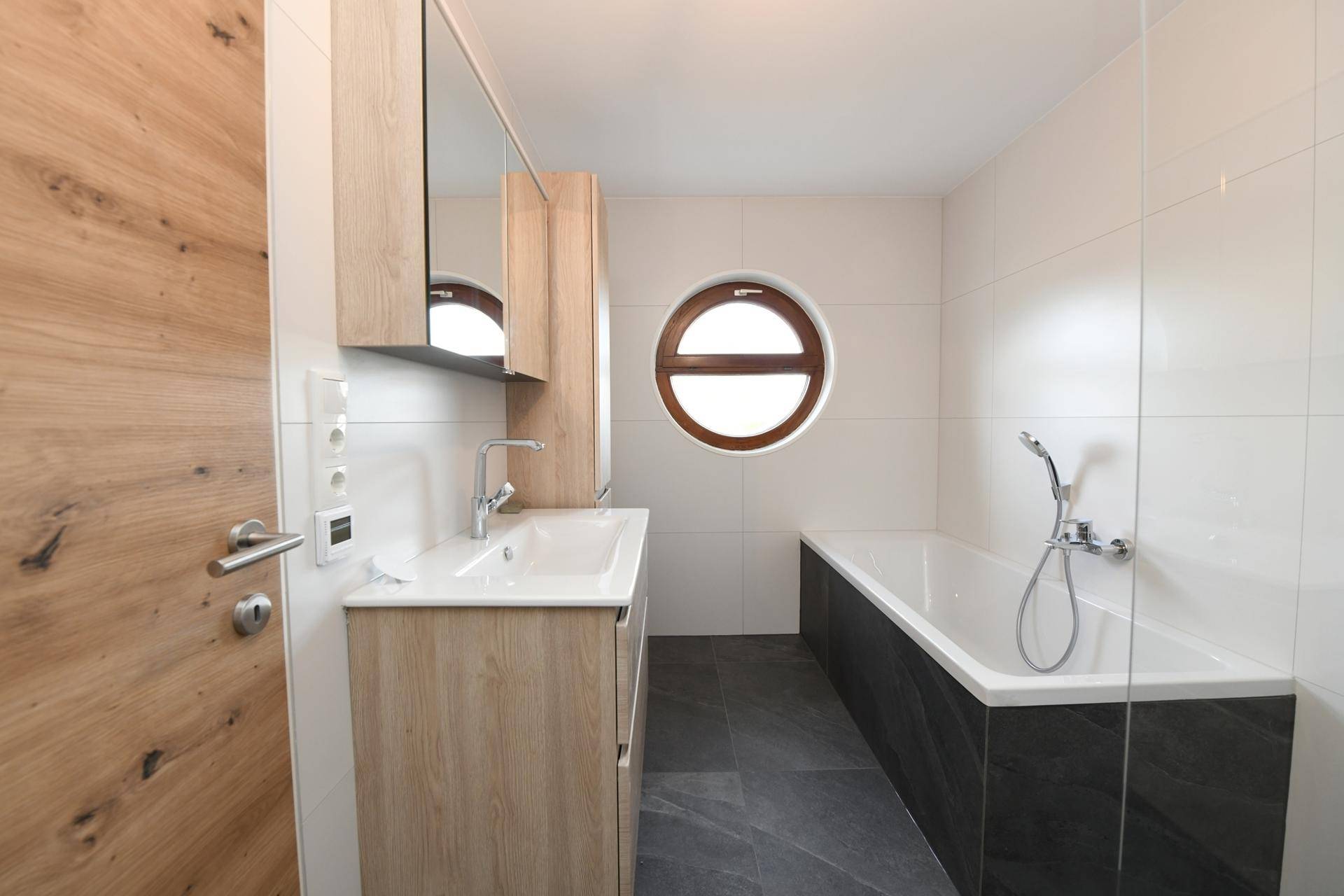 Modernes Badezimmer mit Badewanne, Waschtisch und einem runden Fenster für natürliches Licht.