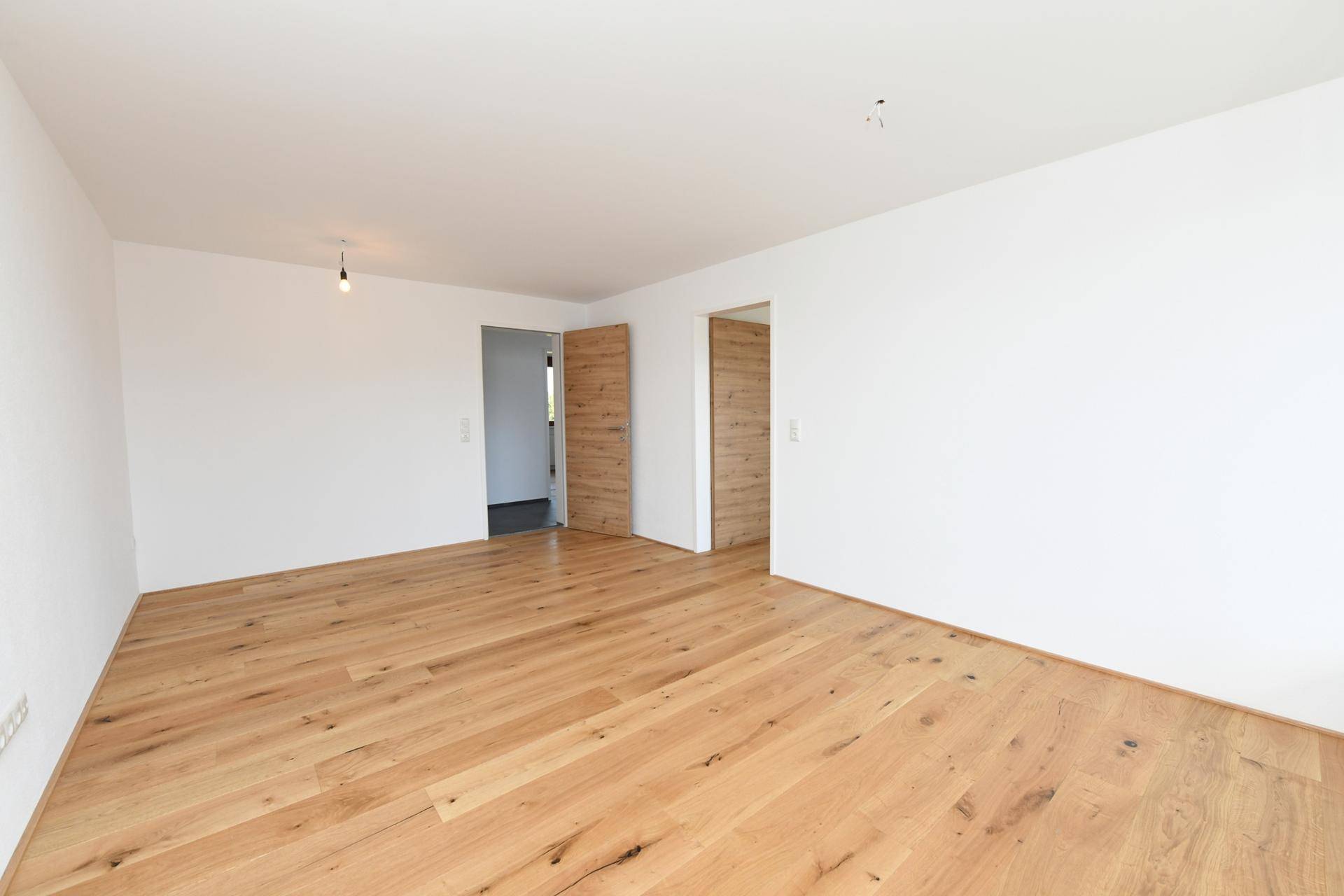 Geräumiges, unmöbliertes Zimmer mit hellem Holzboden und weiß gestrichenen Wänden.