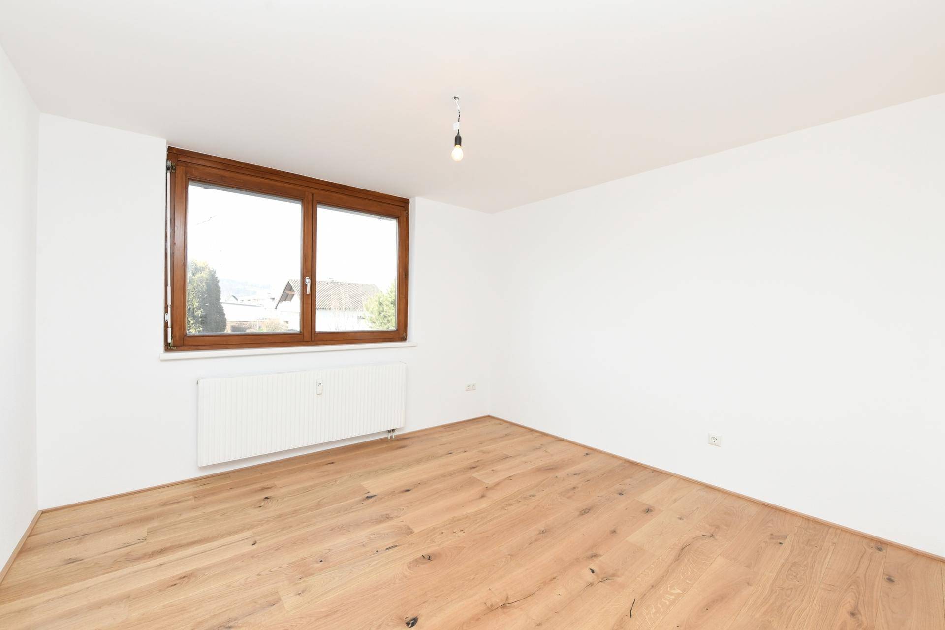 Helles Zimmer mit Holzboden und Fenster, das viel Tageslicht hereinlässt.