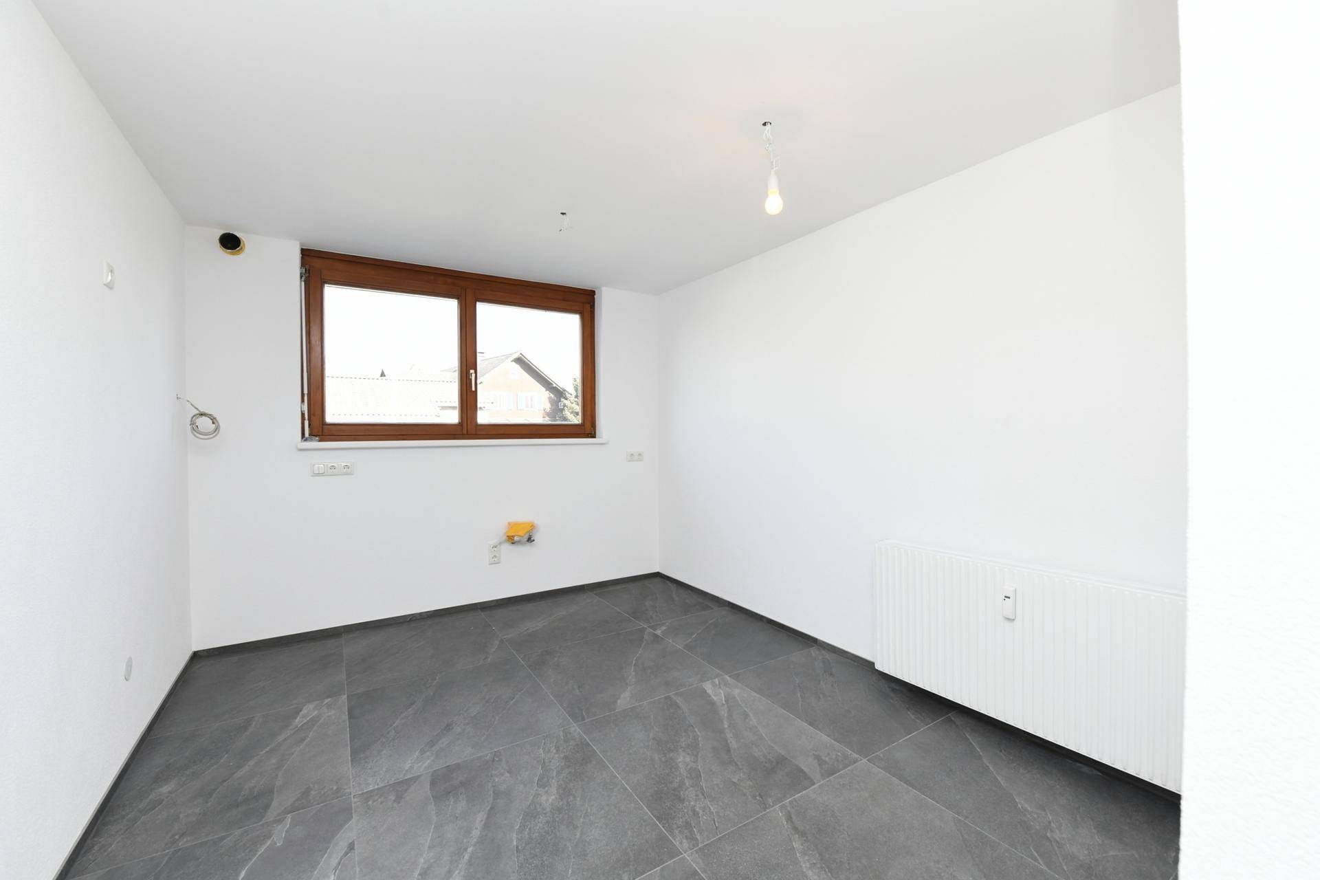 Unmöblierte Küche mit dunklen Fliesen und einem Fenster, das Tageslicht spendet.