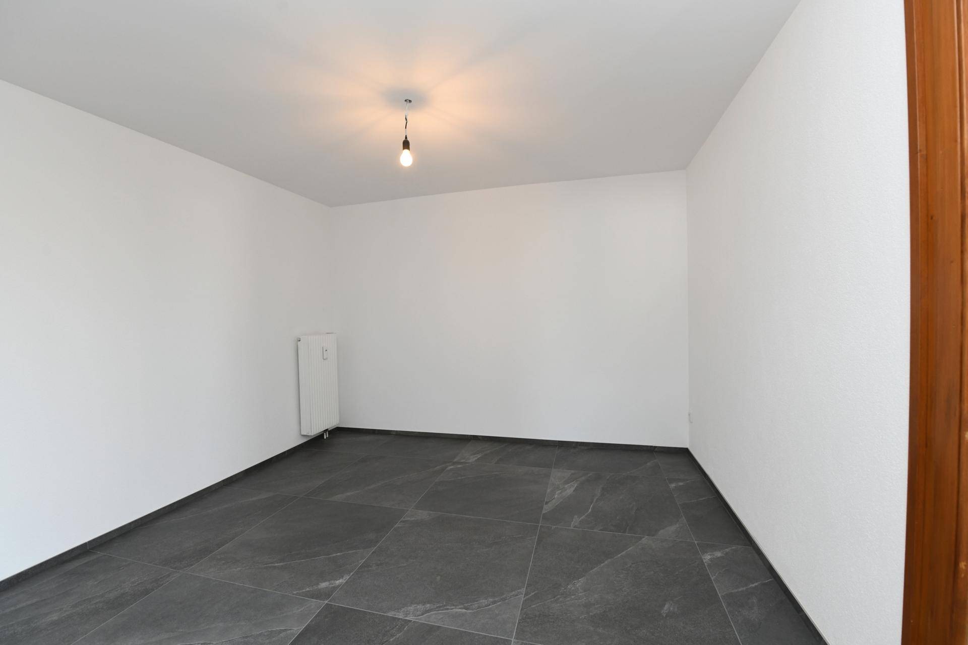 Leeres Zimmer mit dunklen Fliesen und weiß gestrichenen Wänden, ideal als Kinderzimmer.