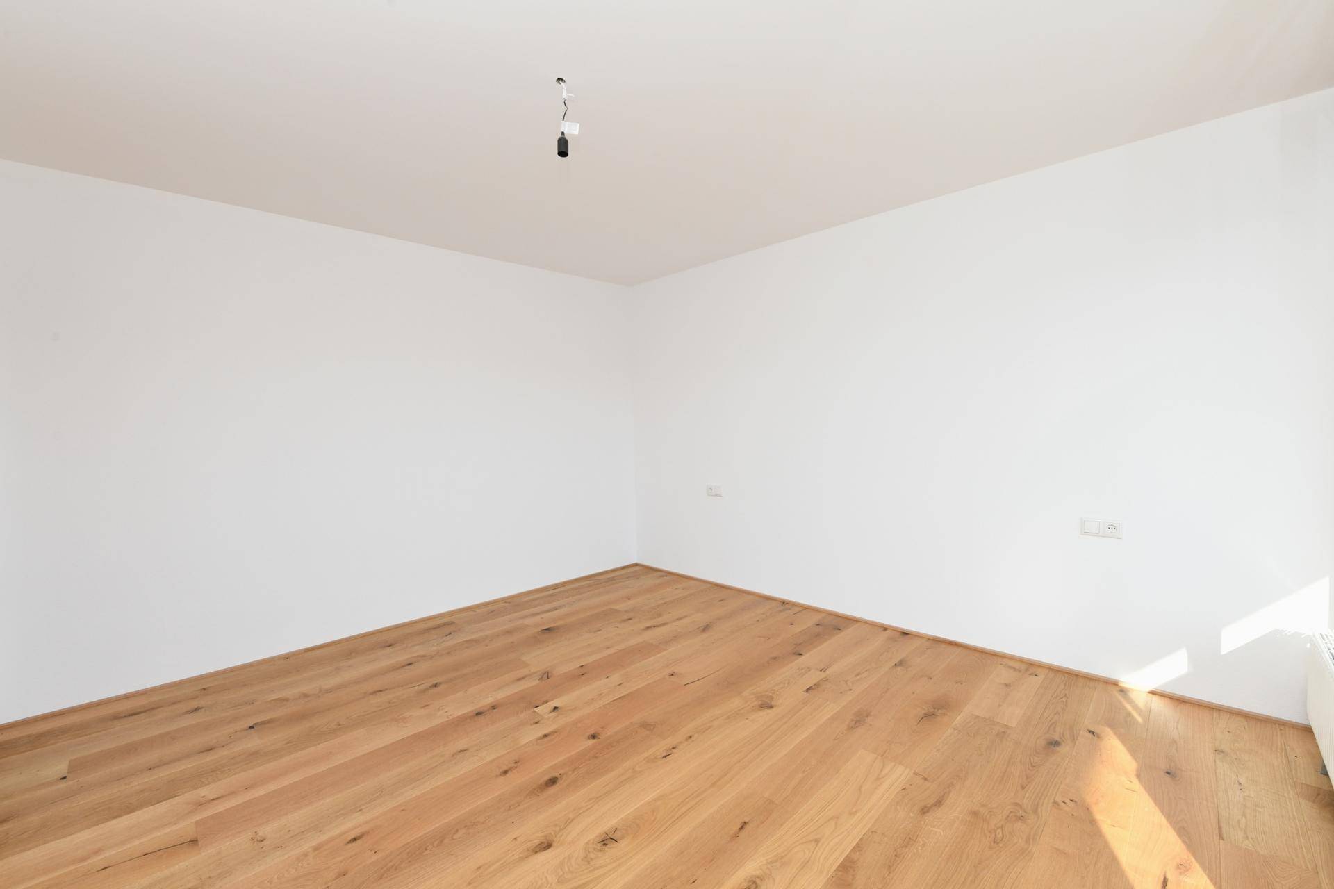 Leeres Zimmer mit hellem Holzboden und weiß gestrichenen Wänden, ideal als Schlafzimmer.