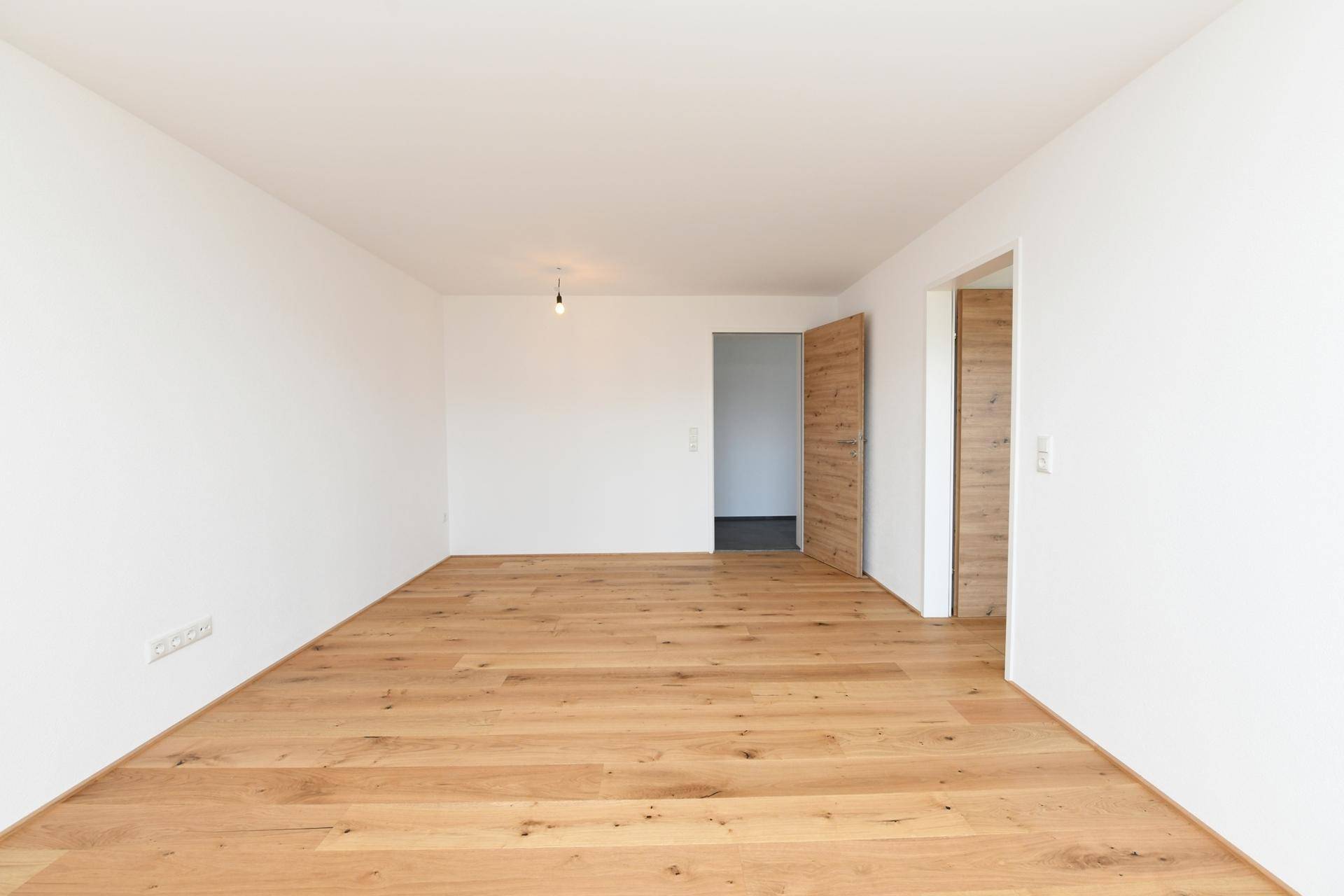 Leerer Raum mit Eichenparkett und weiß gestrichenen Wänden, bereit zur individuellen Gestaltung.