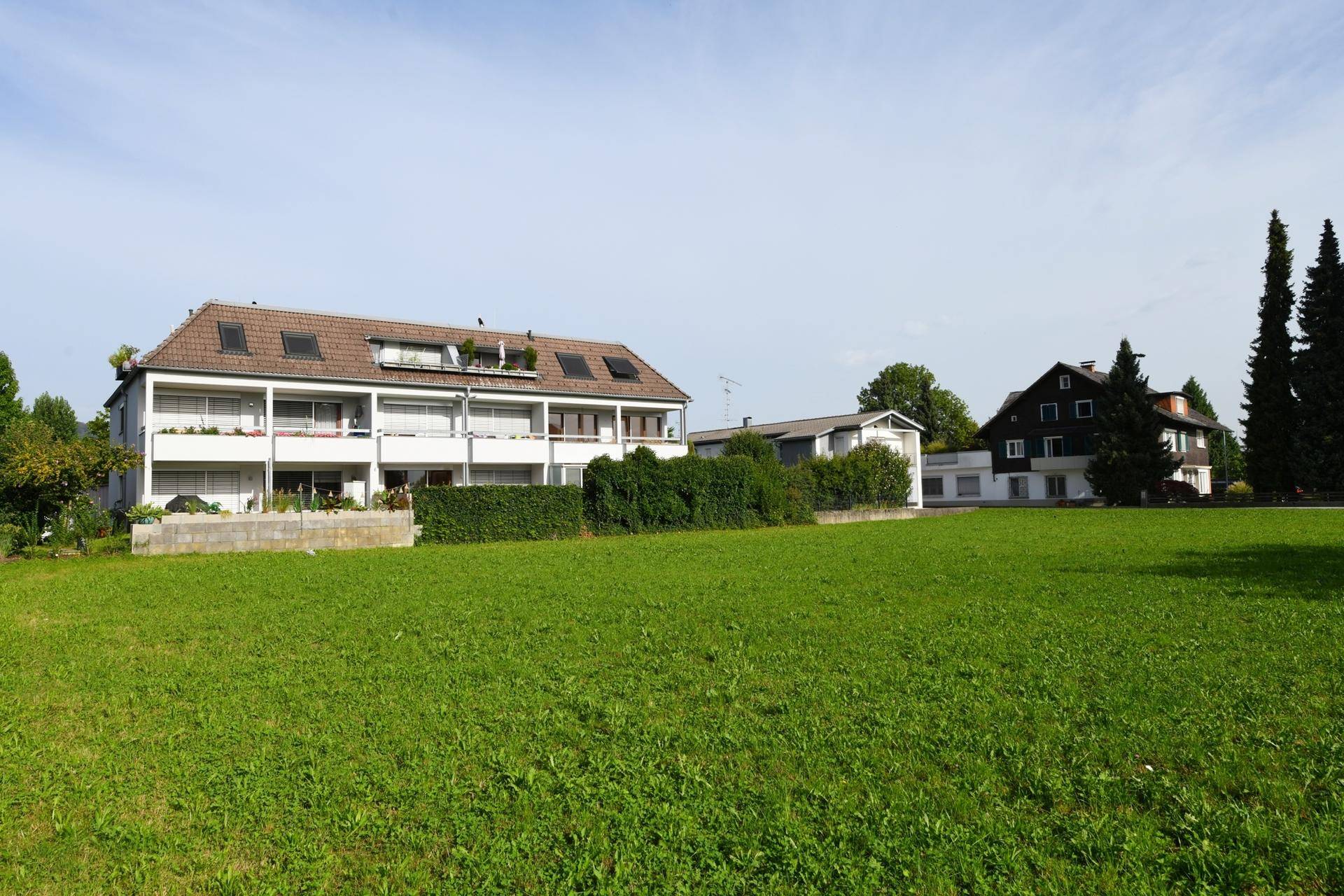 Wohngebäude mit Balkonen und grüner Umgebung, umgeben von weitläufigen Rasenflächen.