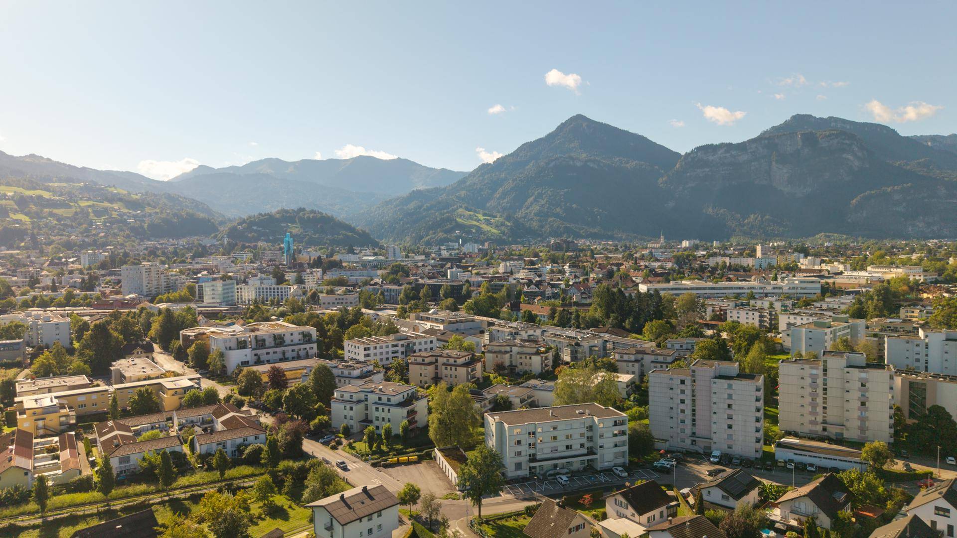 Luftaufnahme einer Wohngegend mit Bergen im Hintergrund unter blauem Himmel.