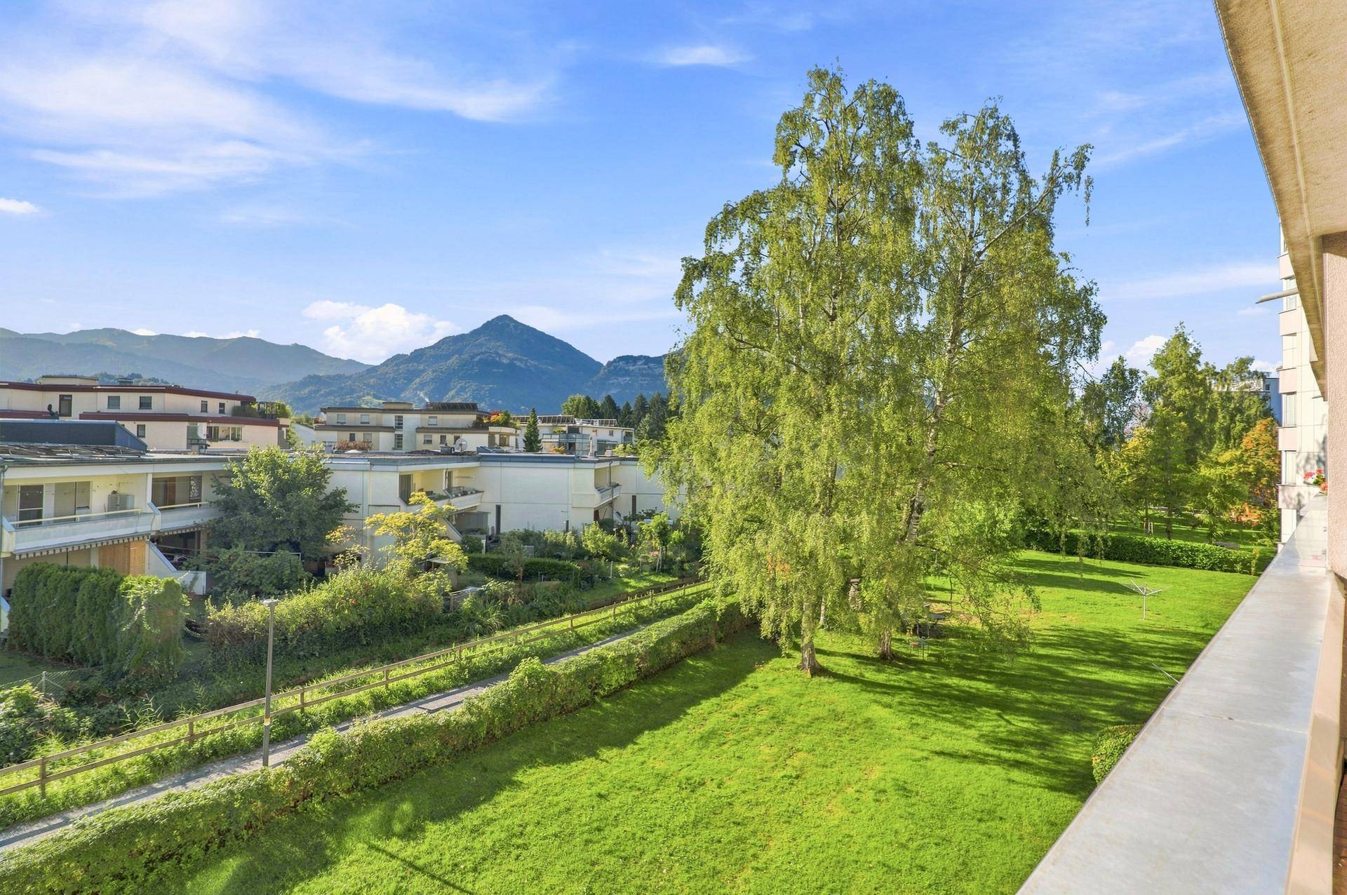 Balkon mit weitem Blick über eine Grünfläche und Berge im Hintergrund.