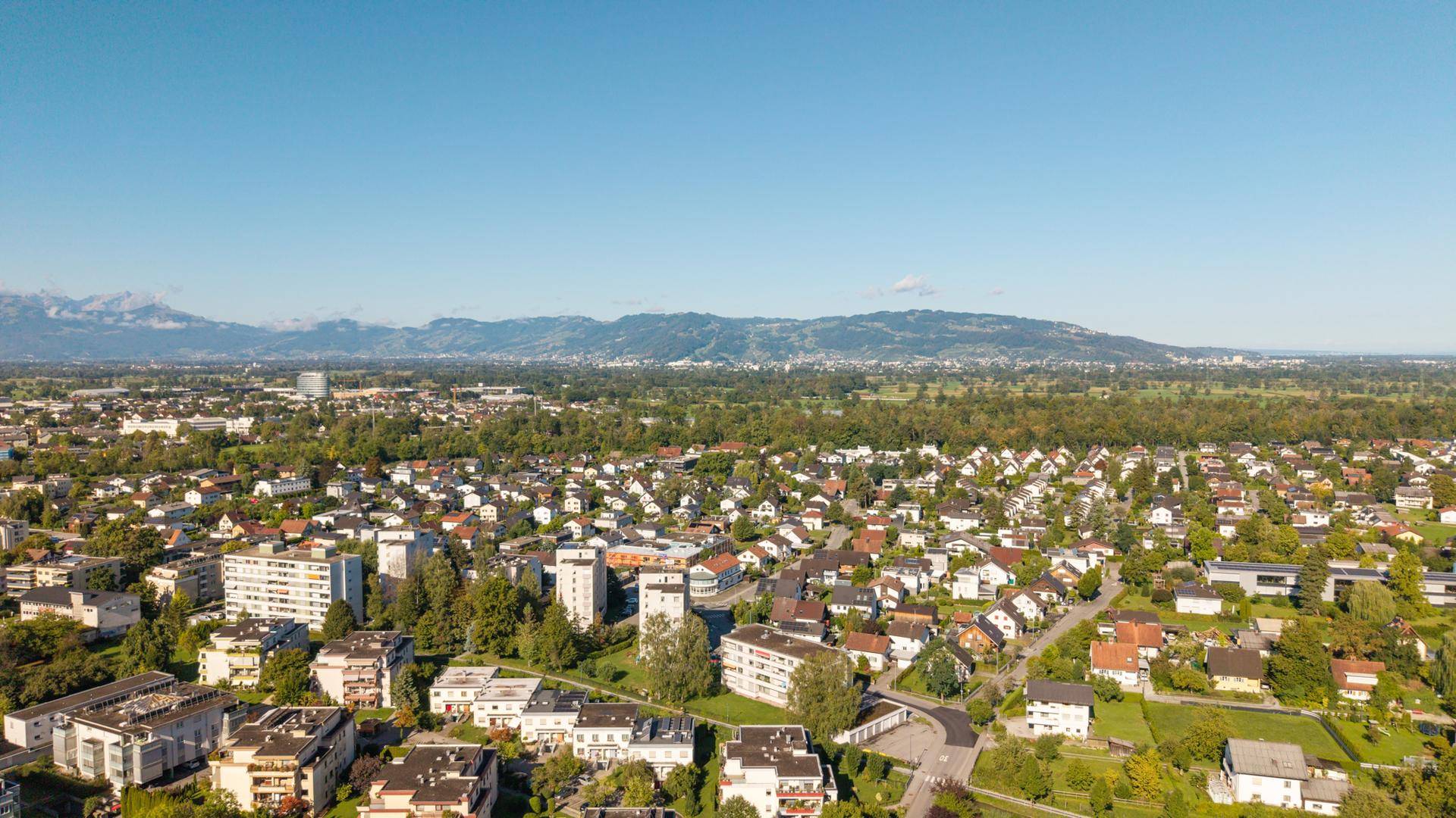 Panoramablick aus der Luft über eine Stadtlandschaft mit Bergen im Hintergrund.