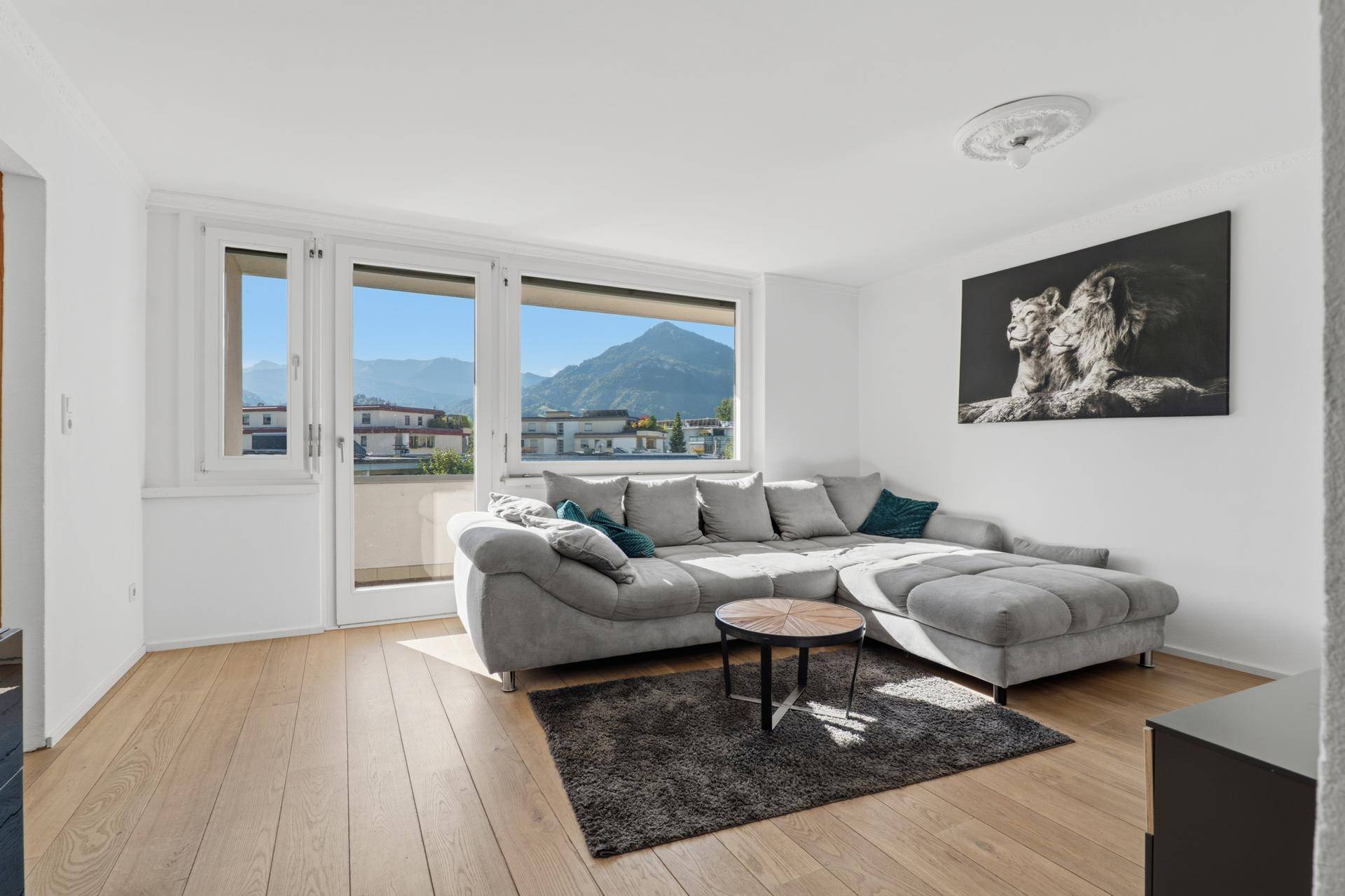 Lichtdurchflutetes Wohnzimmer mit modernem Sofa, Holzboden und Panoramablick auf die Berge.