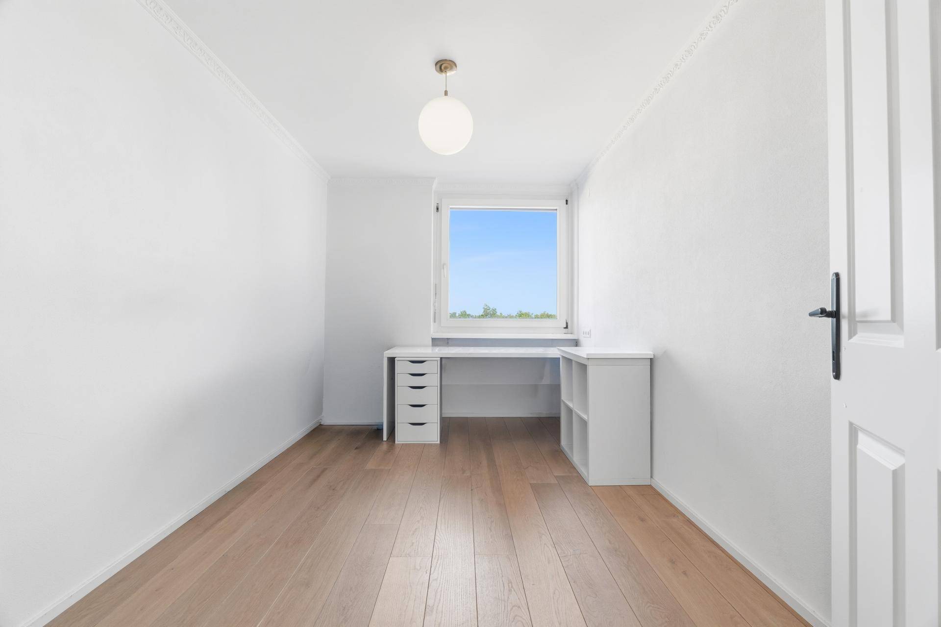 Helles Zimmer mit Schreibtisch, Holzboden und Fenster mit Grünblick.