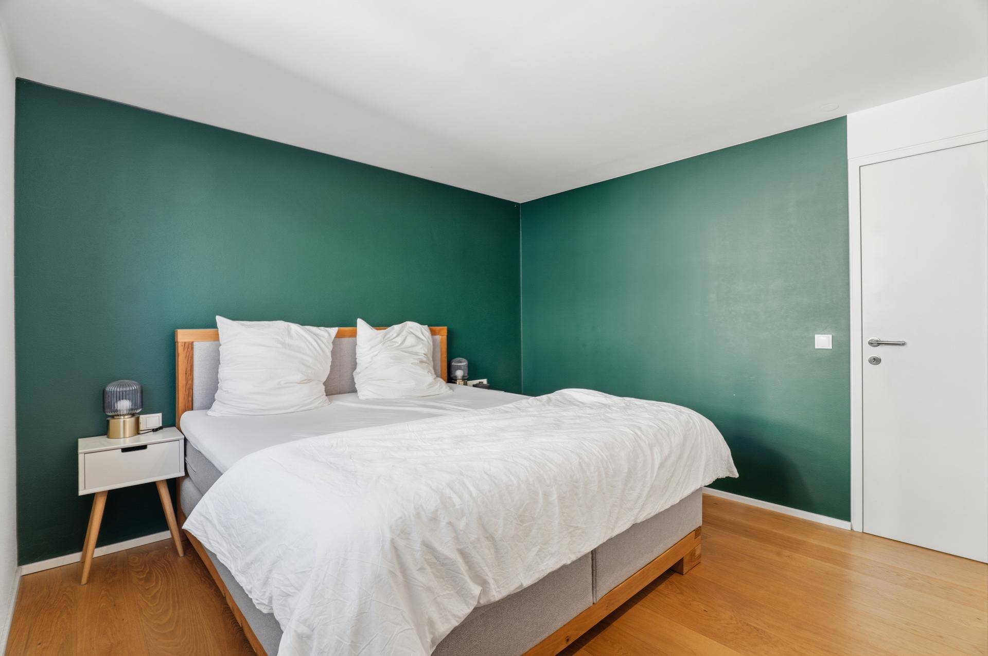 Schlafzimmer mit dunkelgrüner Akzentwand und hellem Holzboden.
