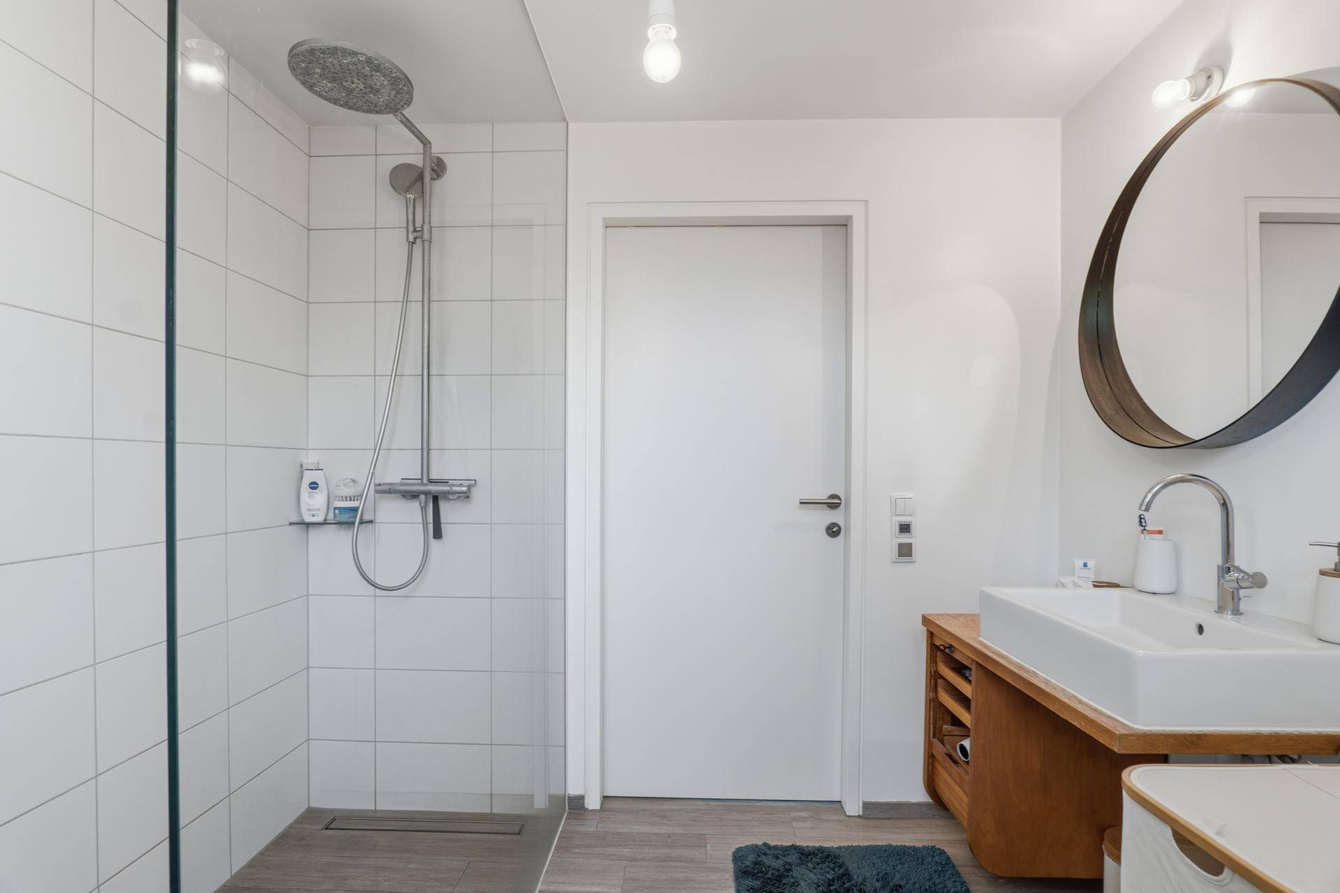 Badezimmer mit großer Regendusche, weißen Fliesen und modernem Waschtisch.