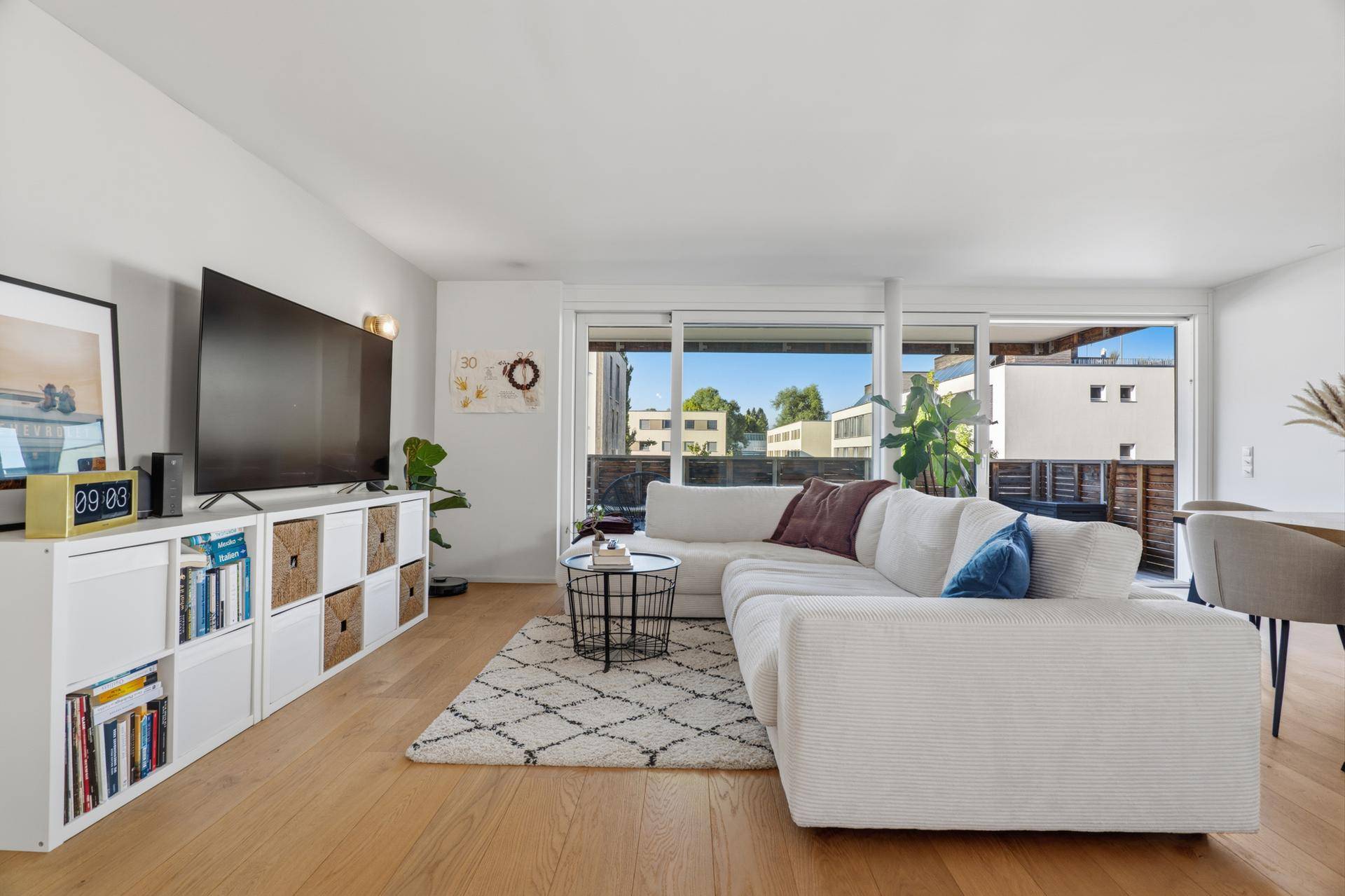 Gemütliches Wohnzimmer mit großem Sofa, Fernseher und Zugang zum Balkon.