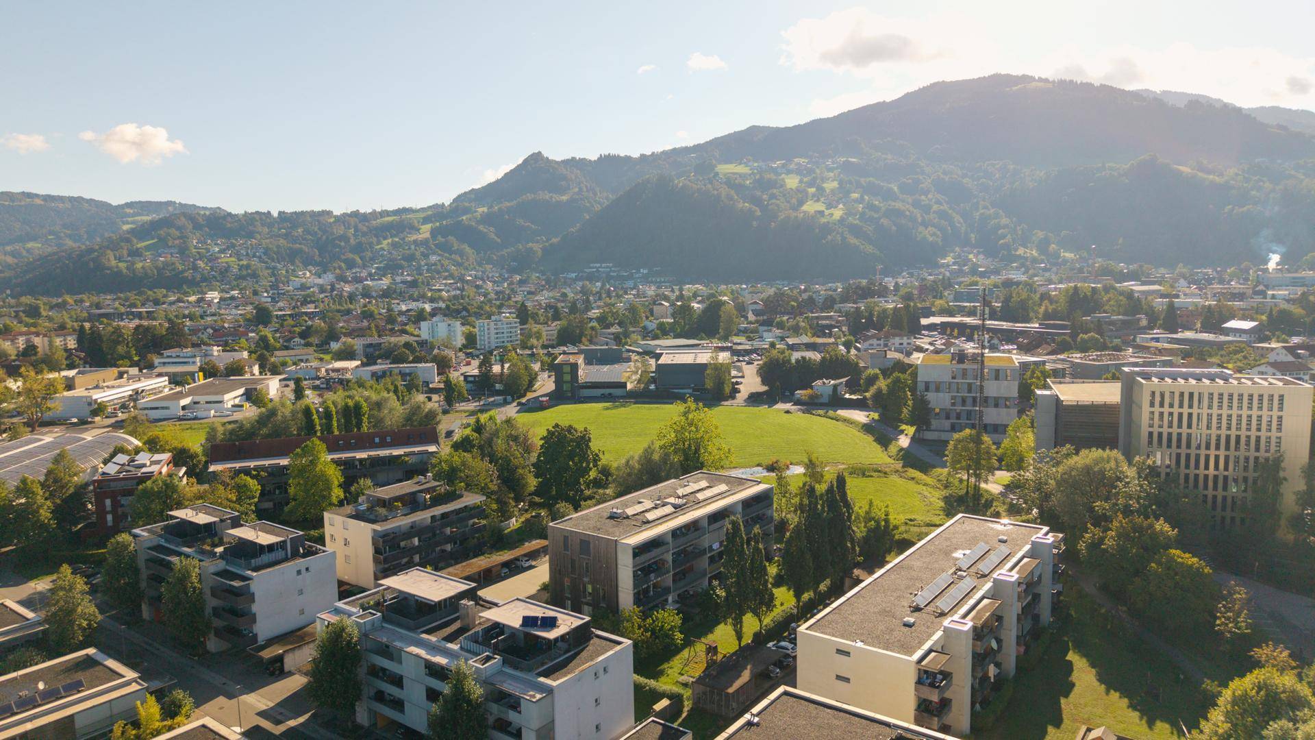 Überblick über die Stadt mit Wohngebieten, Grünflächen und Bergen am Horizont.
