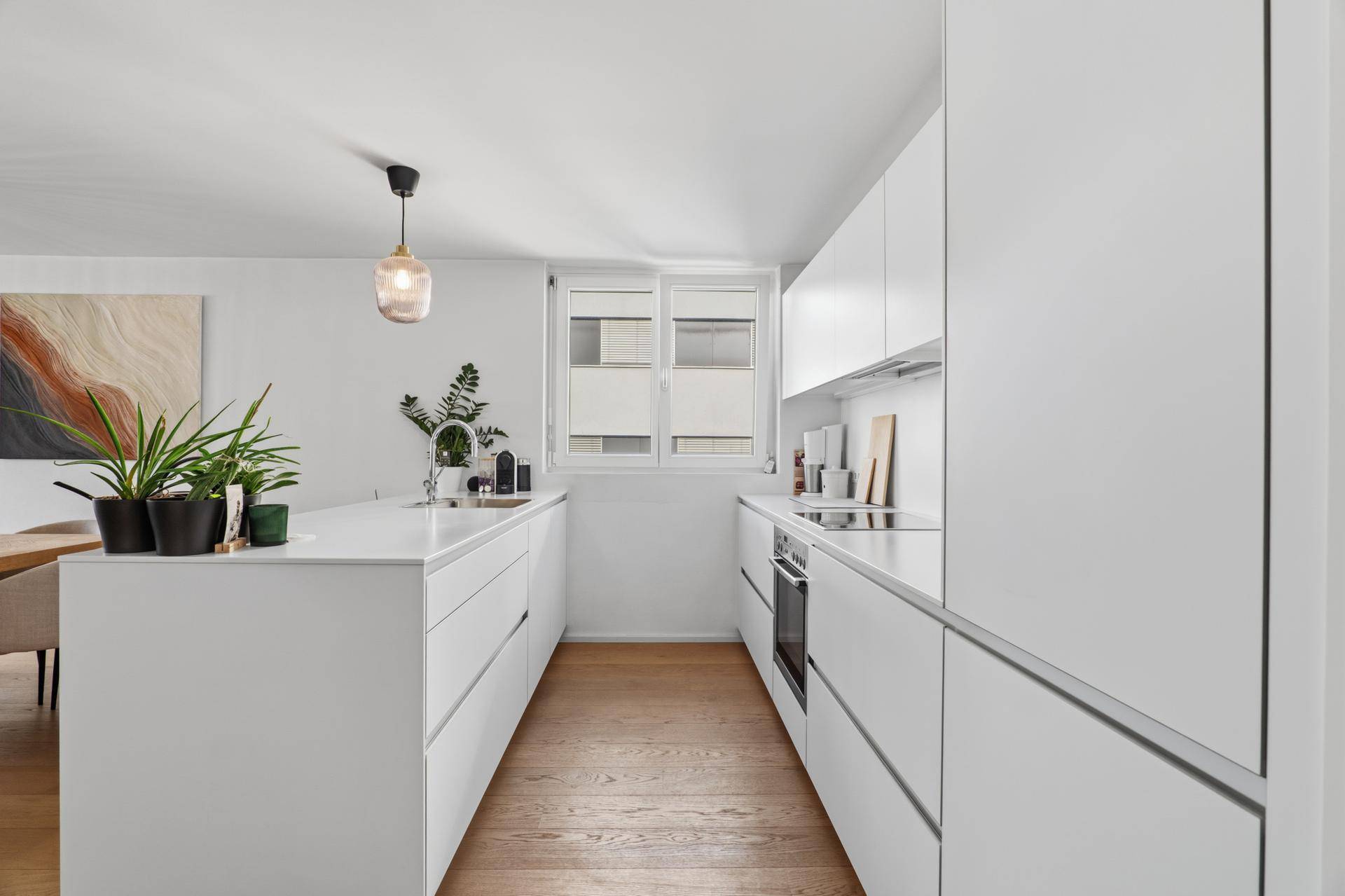 Schmale, moderne Küche mit weißen Schränken, Kochinsel und Fenster.