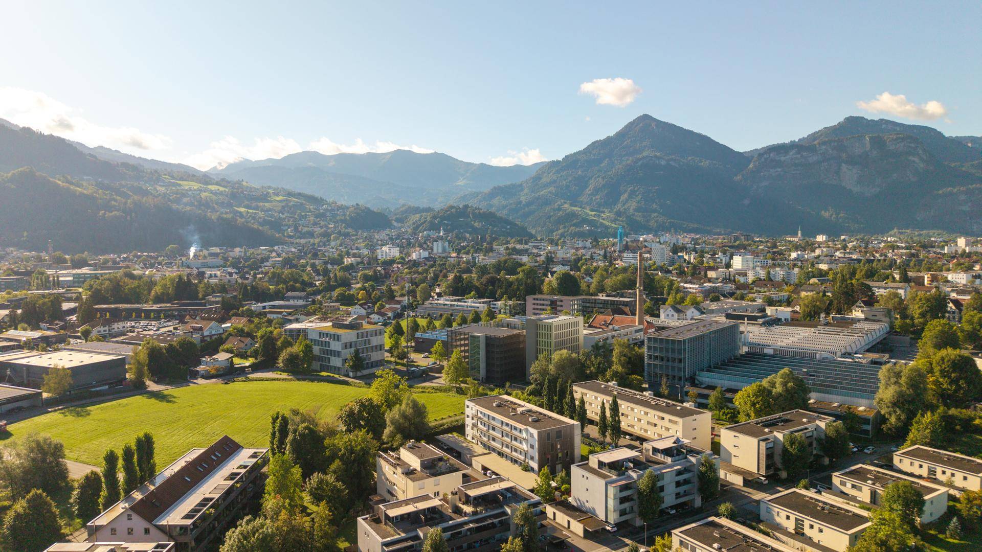 Luftaufnahme der Stadt mit Wohngebäuden und bewaldeten Bergen im Hintergrund.