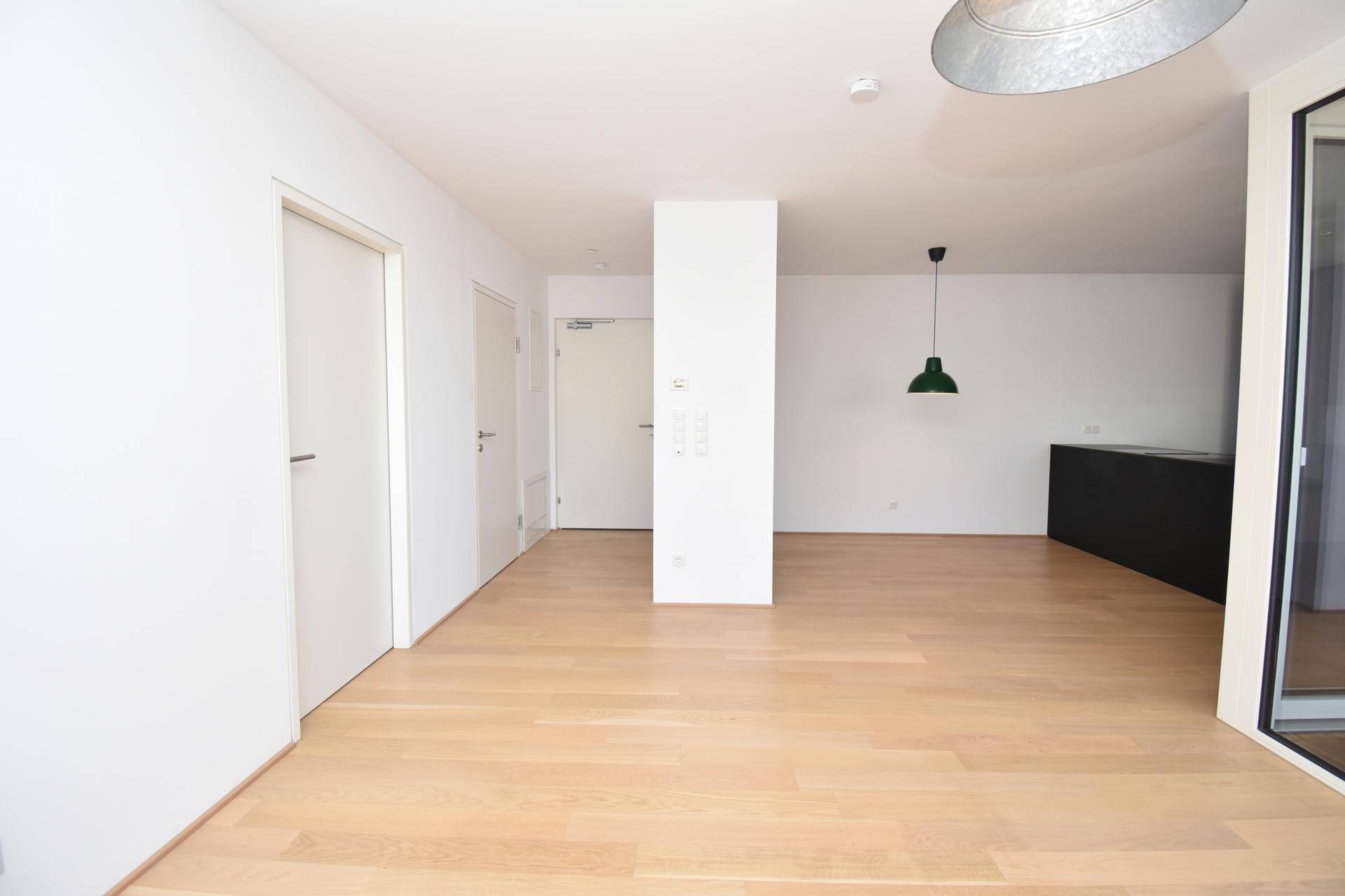 Geräumiger, leerer Wohnbereich mit hellem Parkettboden und Zugang zur modernen Küche.