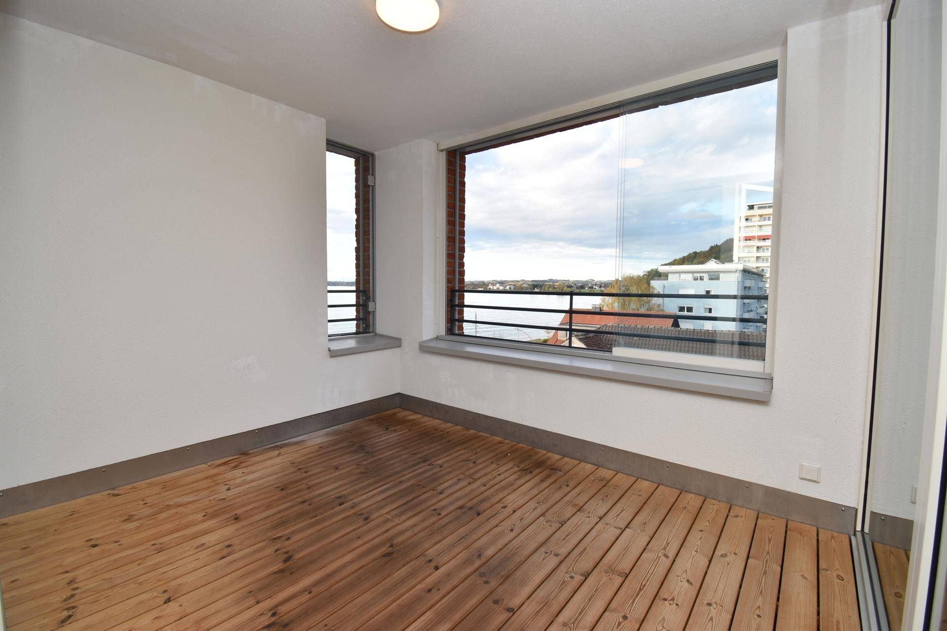 Geräumiger Balkon mit Holzboden und Panoramablick auf den See und die umliegenden Gebäude.