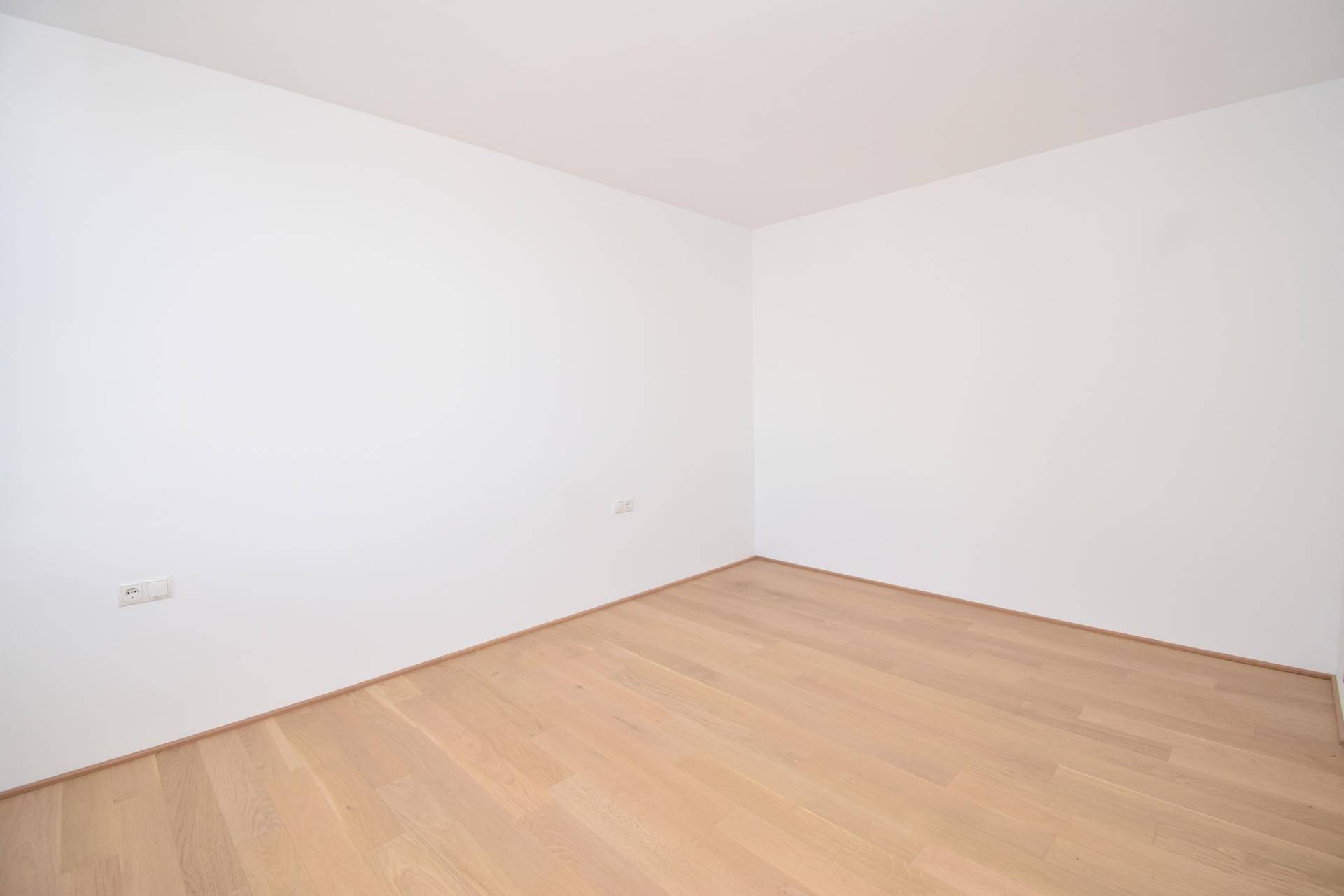 Helles, leeres Zimmer mit Parkettboden und weißen Wänden, bereit zur individuellen Gestaltung.