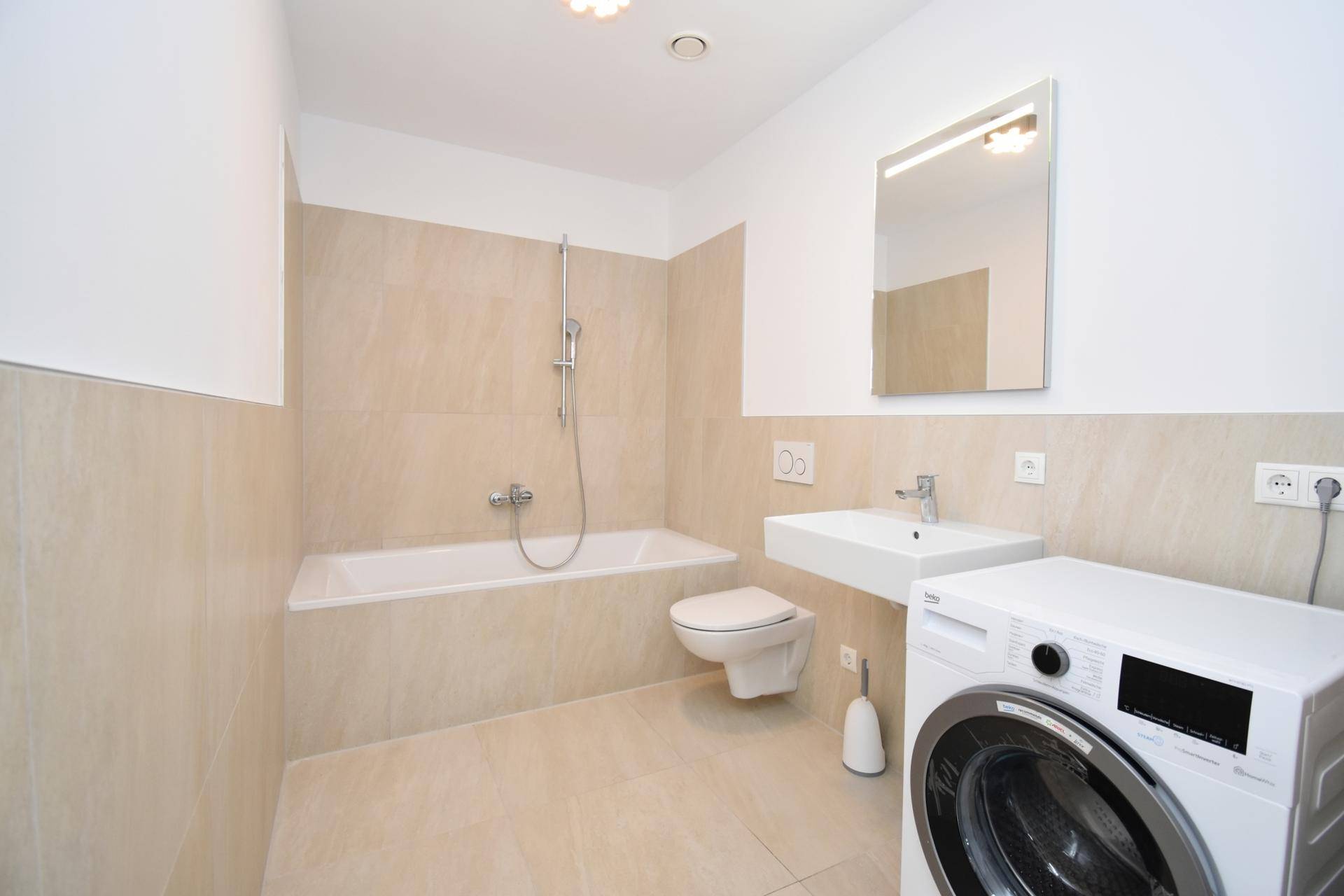 Modernes Badezimmer mit Badewanne, Waschbecken, WC und Waschmaschine, hell gefliest.