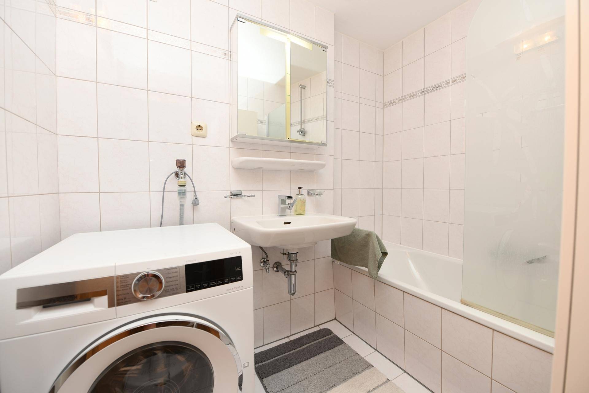 Badezimmer mit Badewanne, Waschbecken und integrierter Waschmaschine.