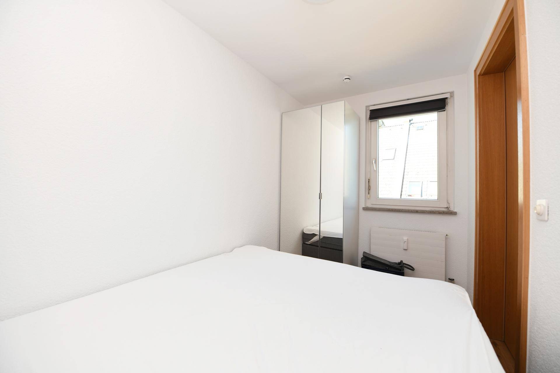 Schlafzimmer mit Doppelbett, Kleiderschrank und Fenster für Tageslicht.