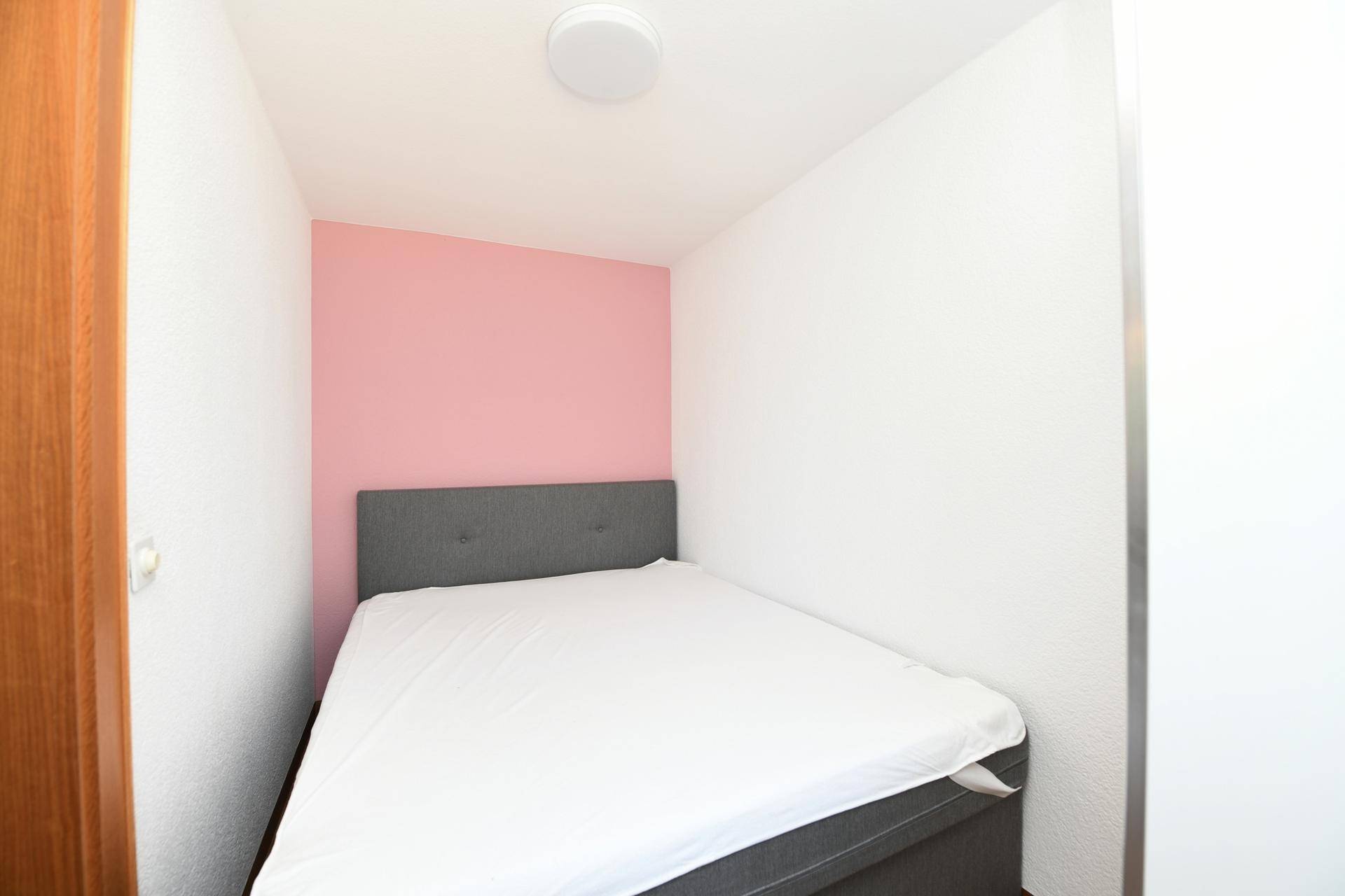 Kleines Schlafzimmer mit Bett und einer farbigen Akzentwand in Rosa.