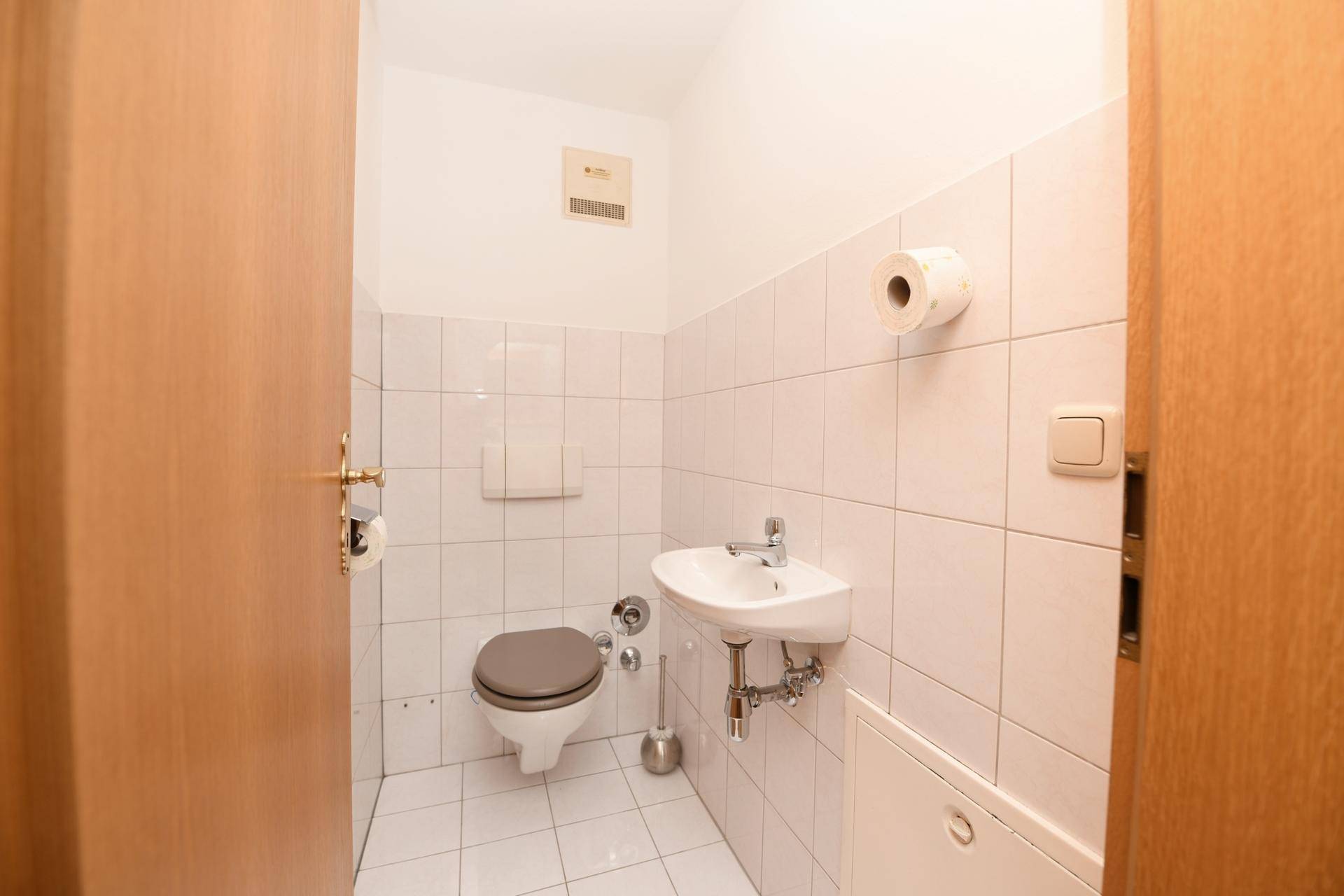 Separates WC mit Toilette, kleinem Waschbecken und weißen Fliesen.