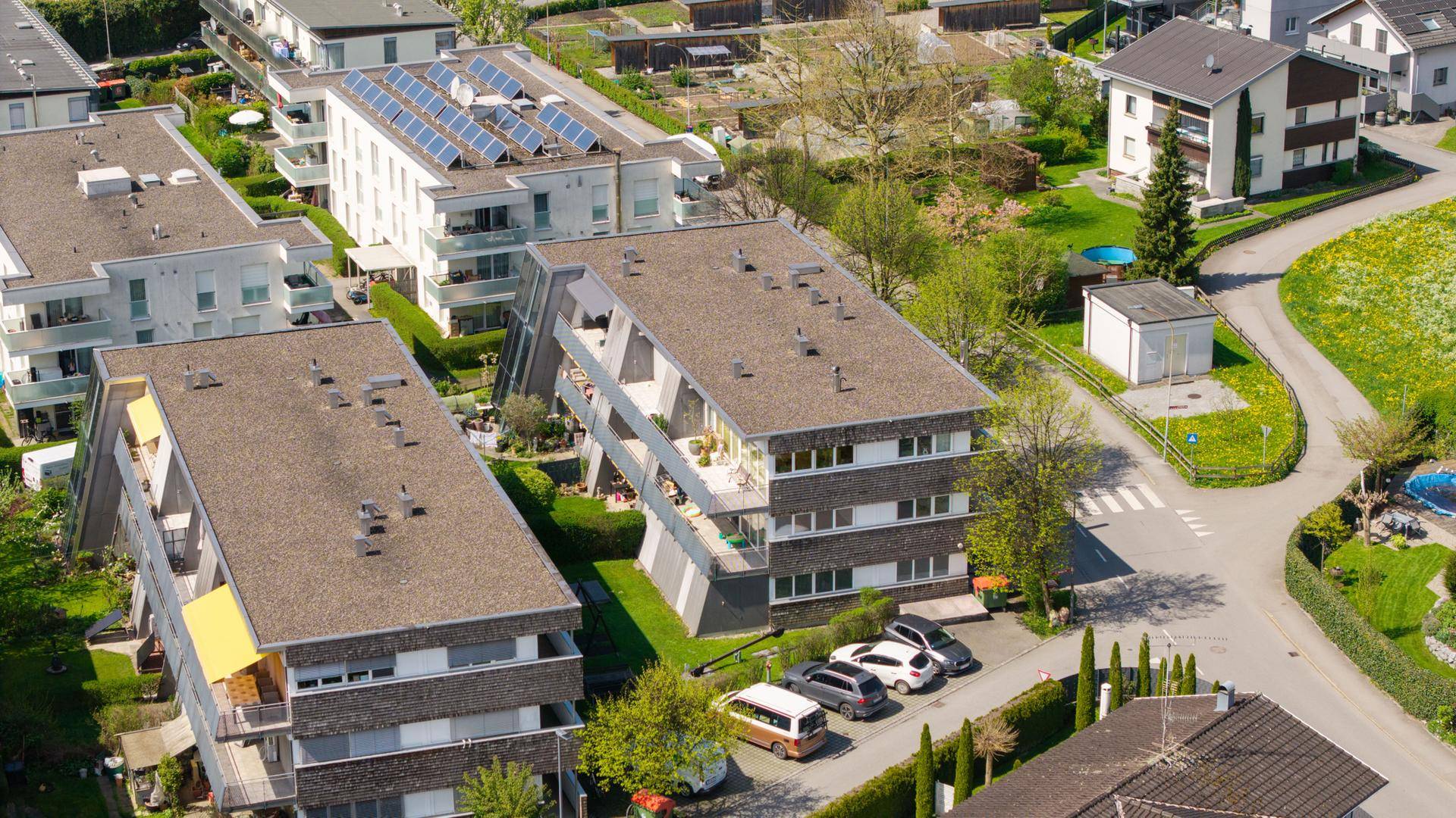 Luftaufnahme einer Wohnsiedlung mit Gebäuden, Grünflächen und Solaranlagen auf Dächern.