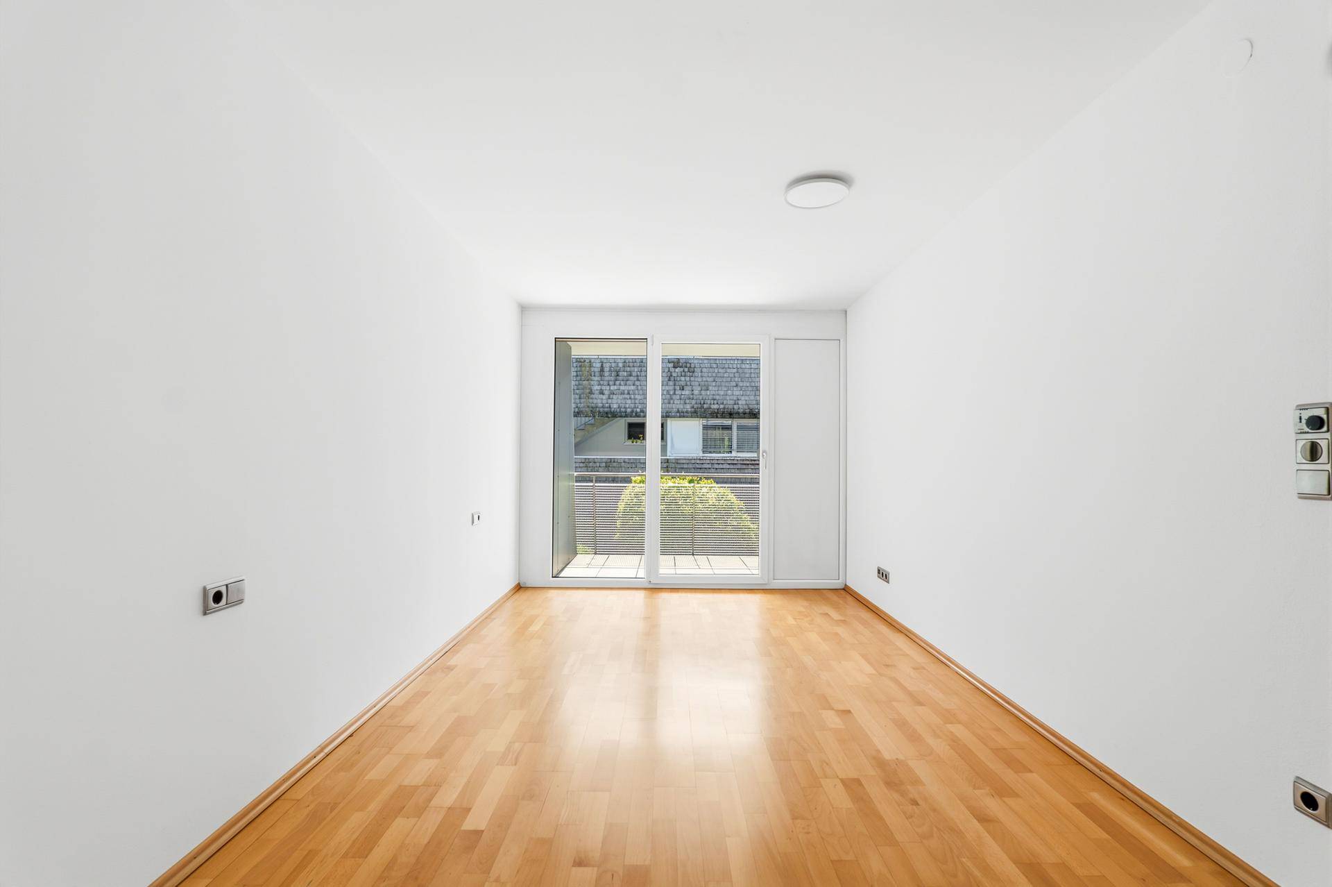 Helles Schlafzimmer mit Parkettboden und Zugang zu einem kleinen Balkon.