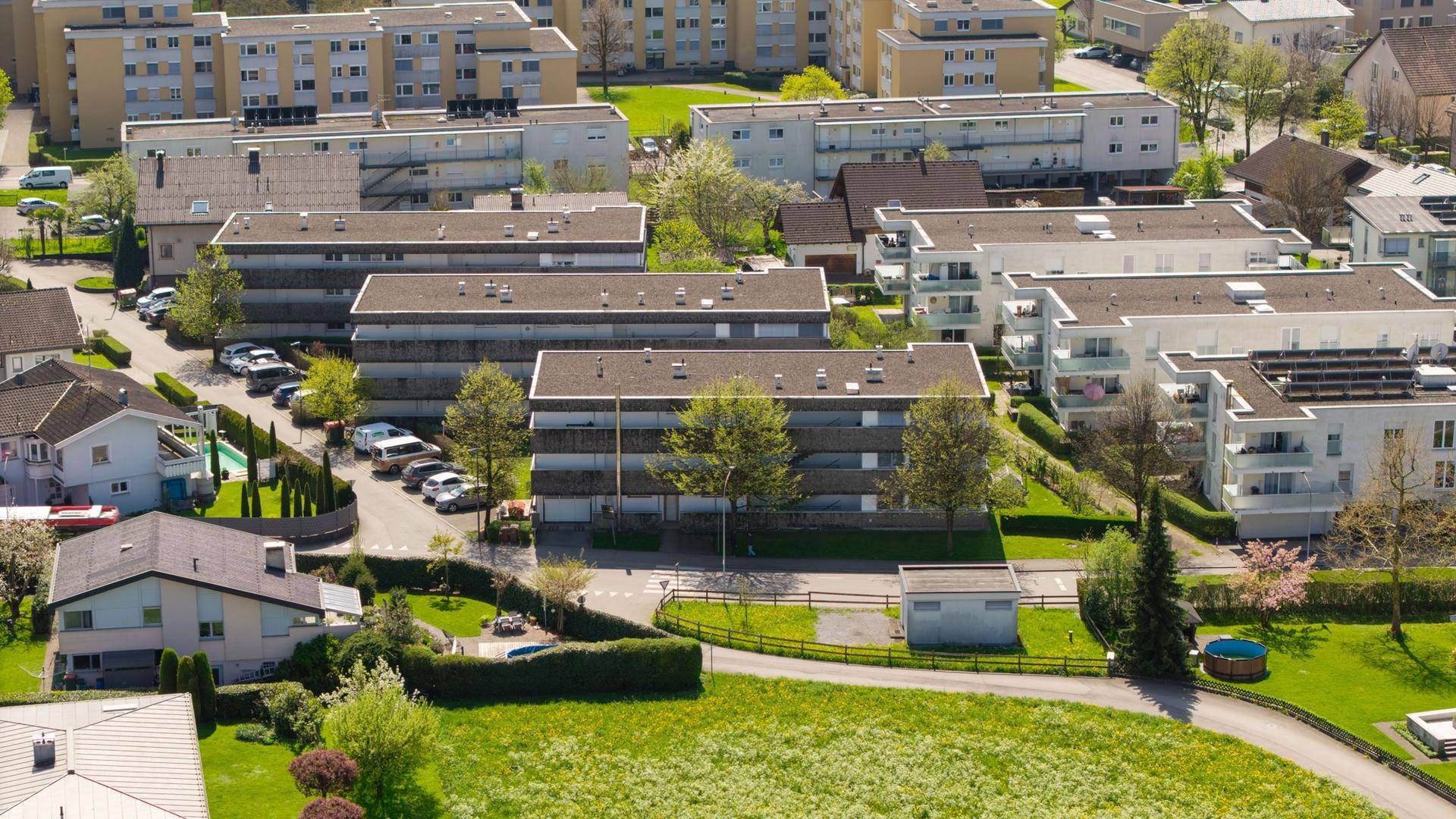 Weitläufige Luftaufnahme einer Wohngegend mit verschiedenen Gebäudetypen und viel Grün.