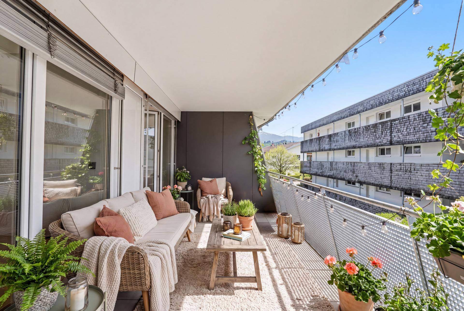 Gemütlicher Balkon mit Outdoor-Möbeln, Pflanzen und Lichterkette.