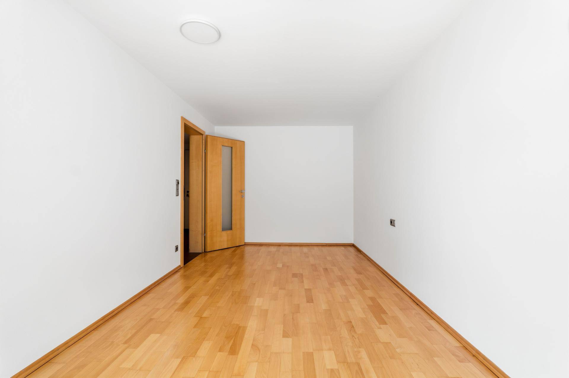 Leeres Schlafzimmer mit hellem Parkettboden und Holztür.