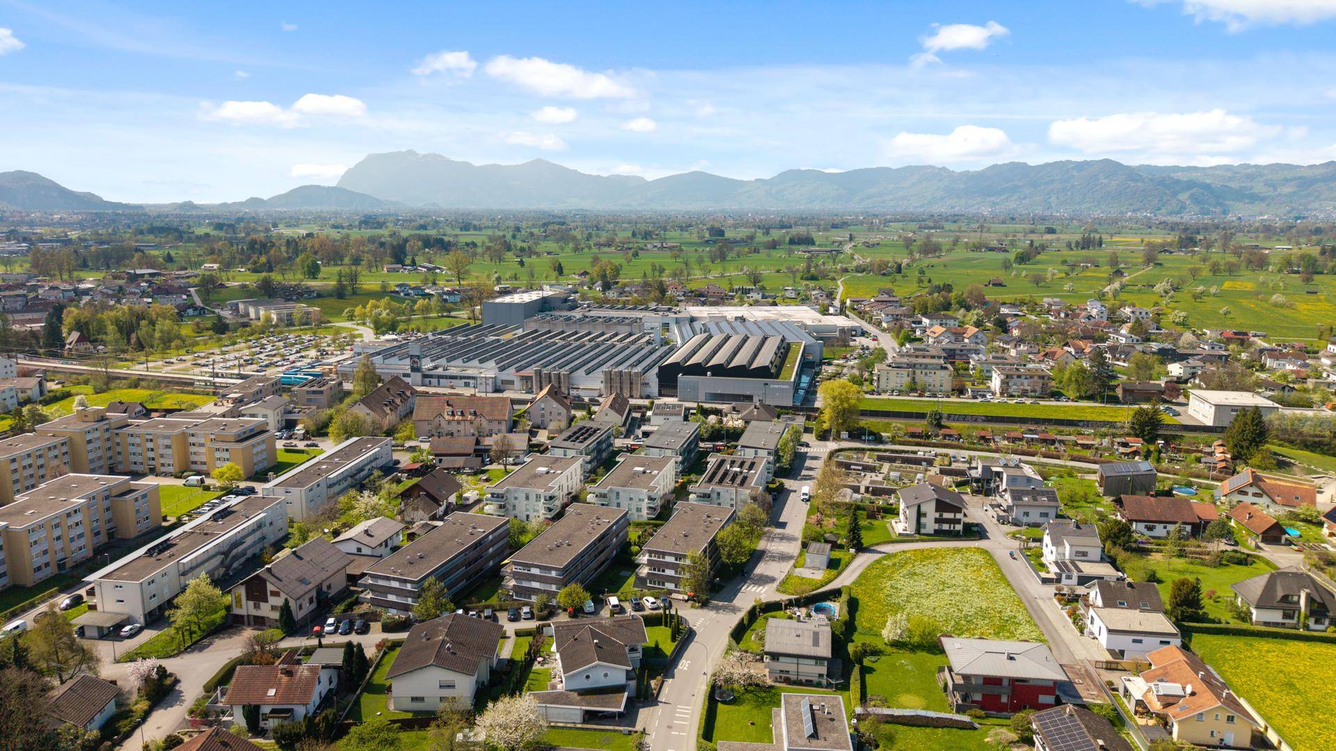 Weitläufige Luftaufnahme einer Stadt mit Industriegebiet und Bergen im Hintergrund.