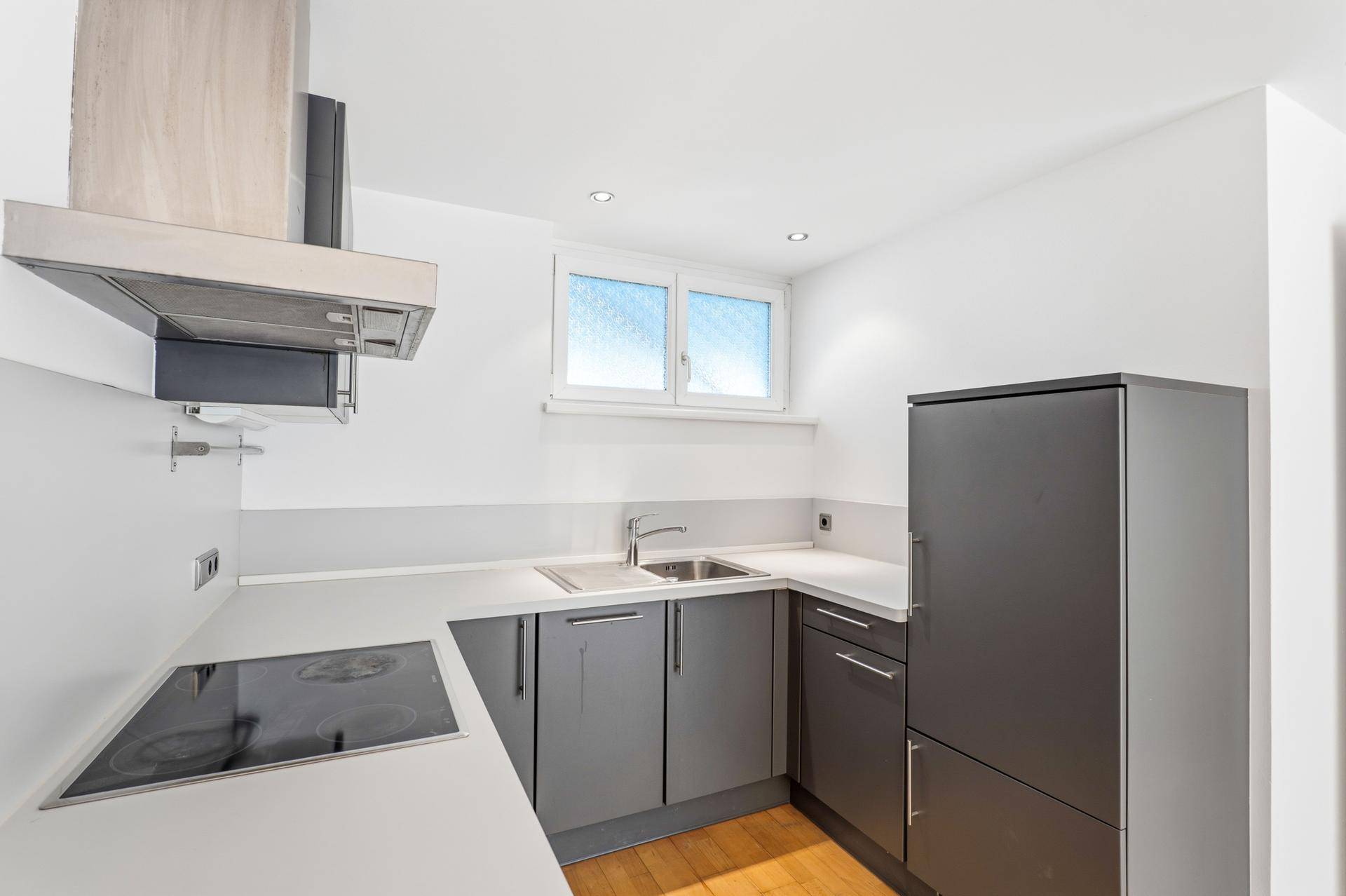 Moderne, graue Küchenzeile mit Induktionskochfeld, Spüle und Kühlschrank.