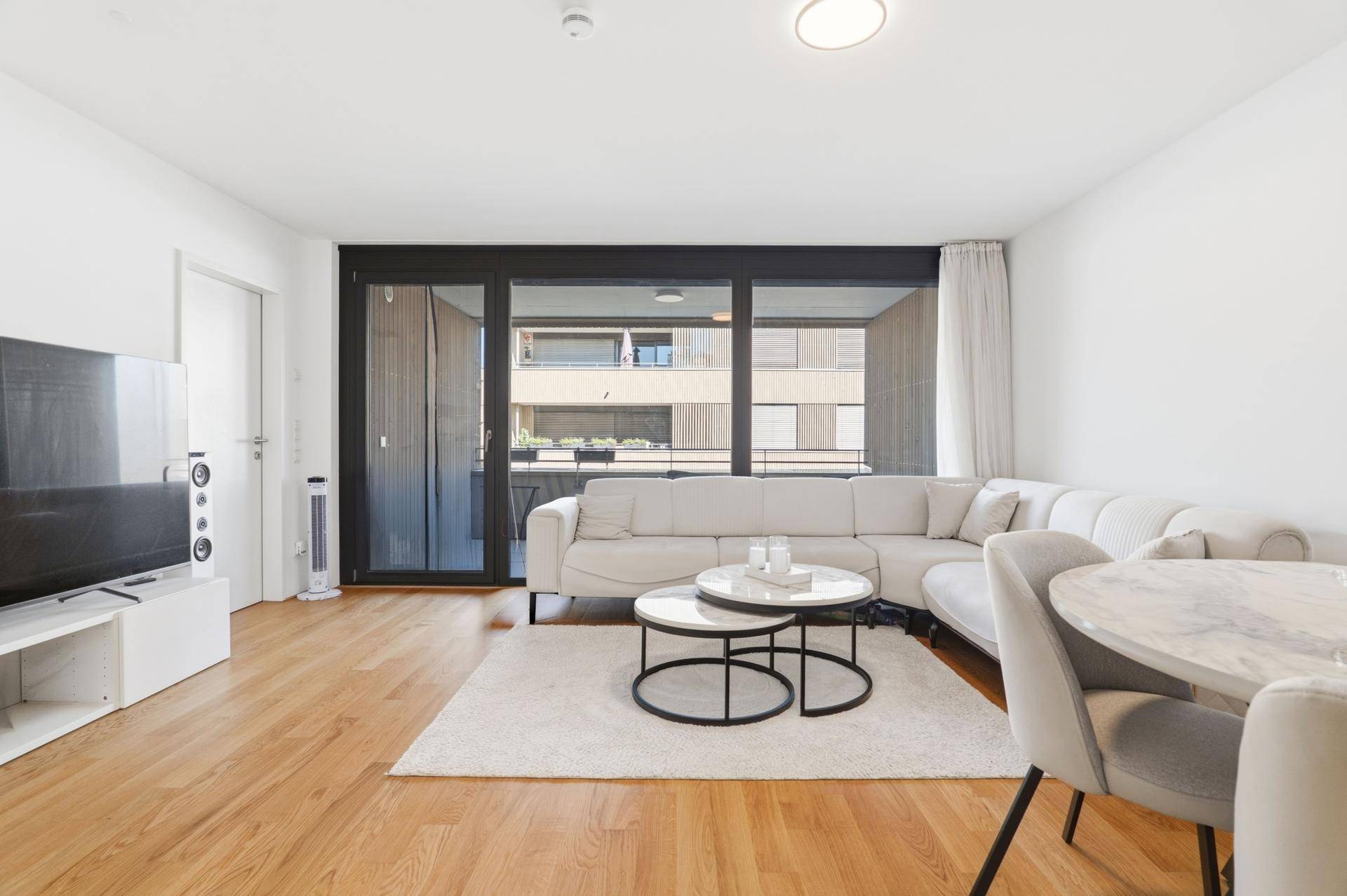 Geräumiger Wohnbereich mit Holzboden, großem Fenster und modernem Mobiliar.