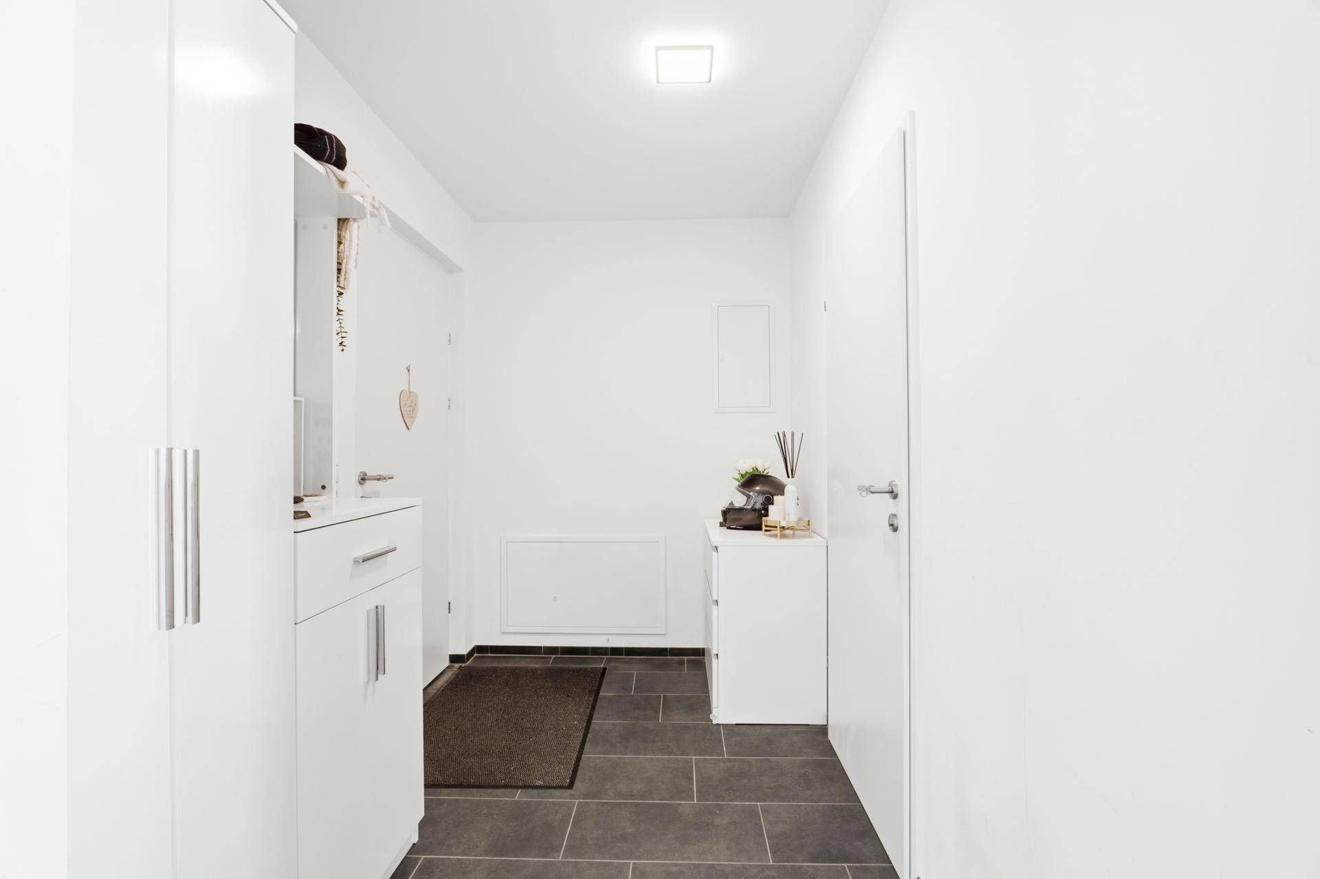 Heller Flur mit dunklen Fliesen, Garderobe und weißer Wandgestaltung.