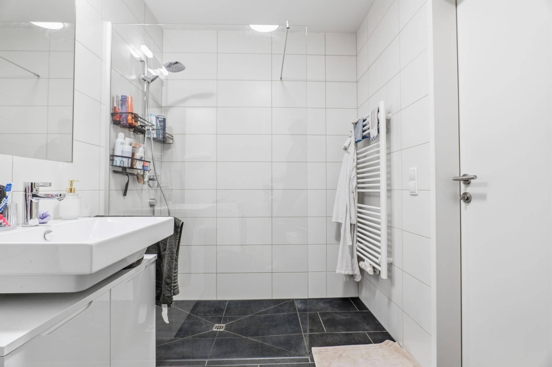 Modernes Badezimmer mit großer begehbarer Dusche und weißen Fliesen.