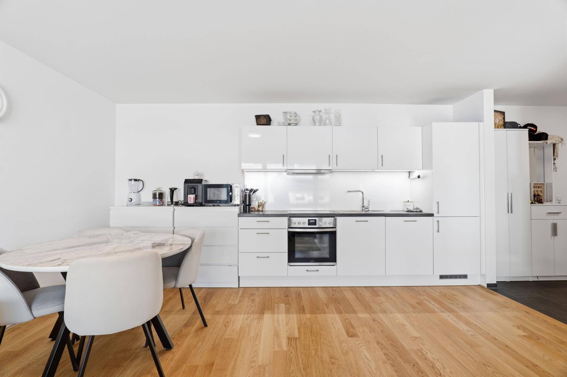 Moderne weiße Einbauküche mit glänzenden Fronten und dunkler Arbeitsplatte.