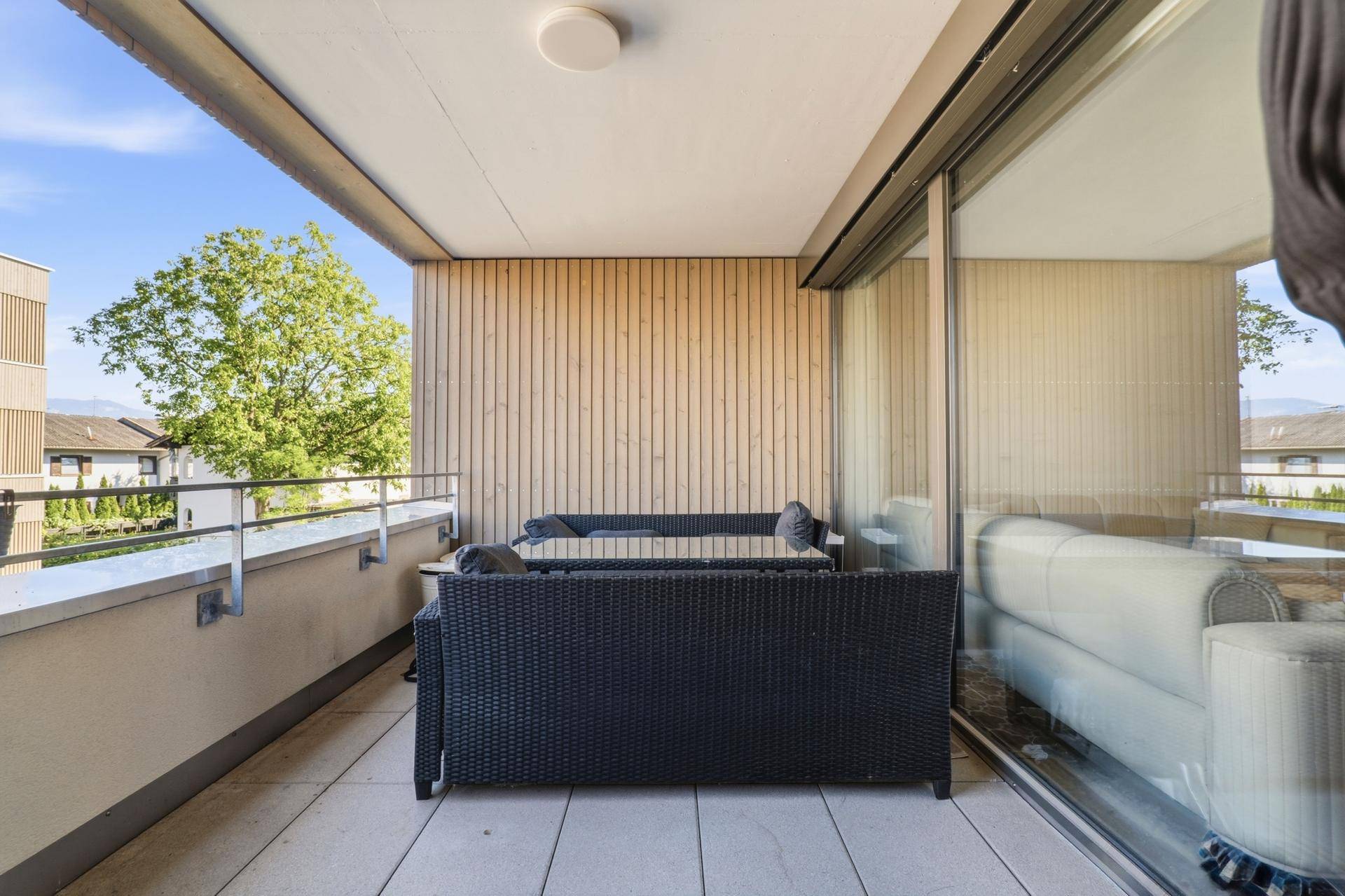 Heller Balkon mit Holzwand, Sitzmöbeln und Blick auf die umliegenden Gebäude.