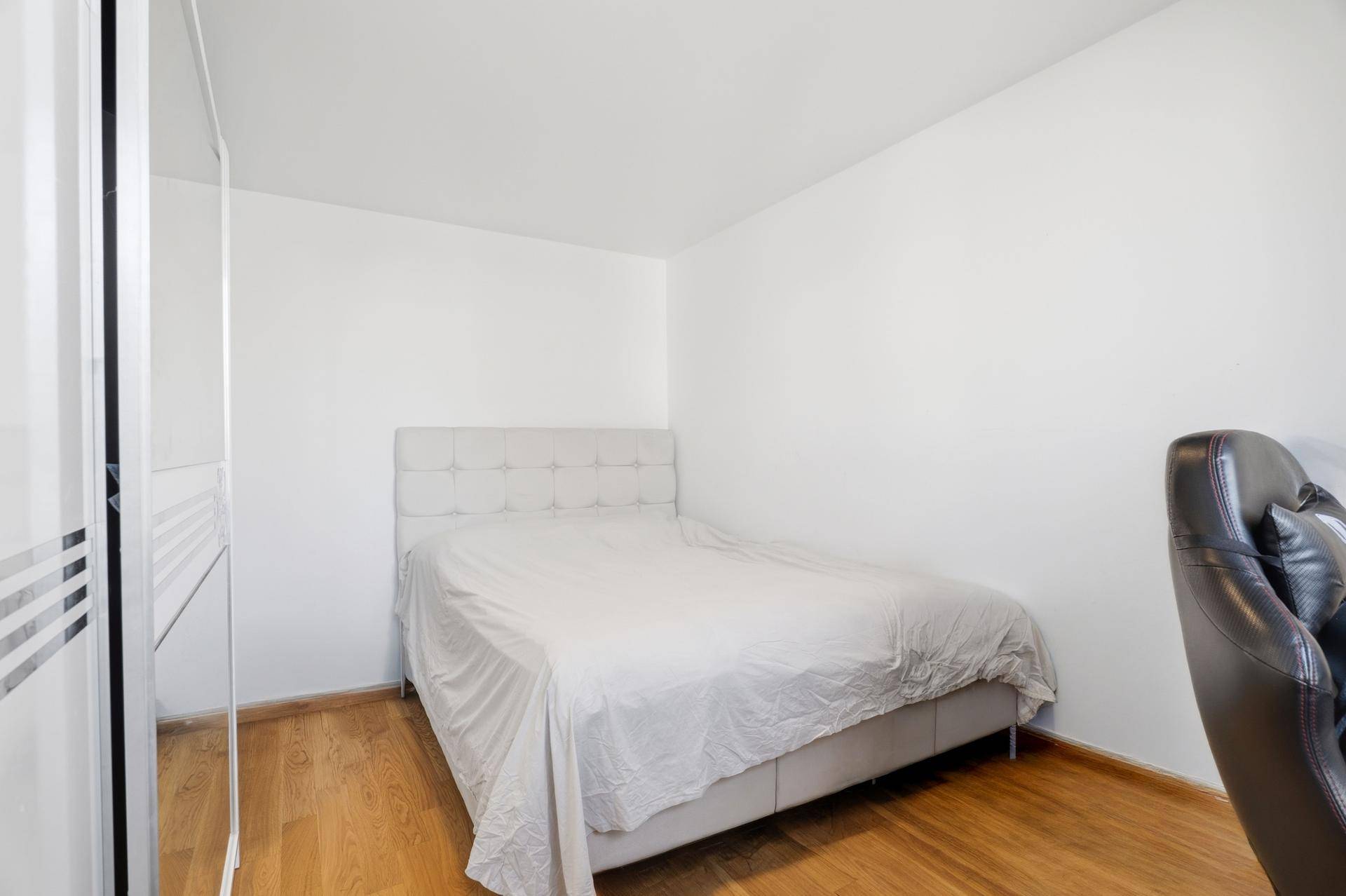Schlafzimmer mit Holzboden, weißem Bett und modernem Kleiderschrank.