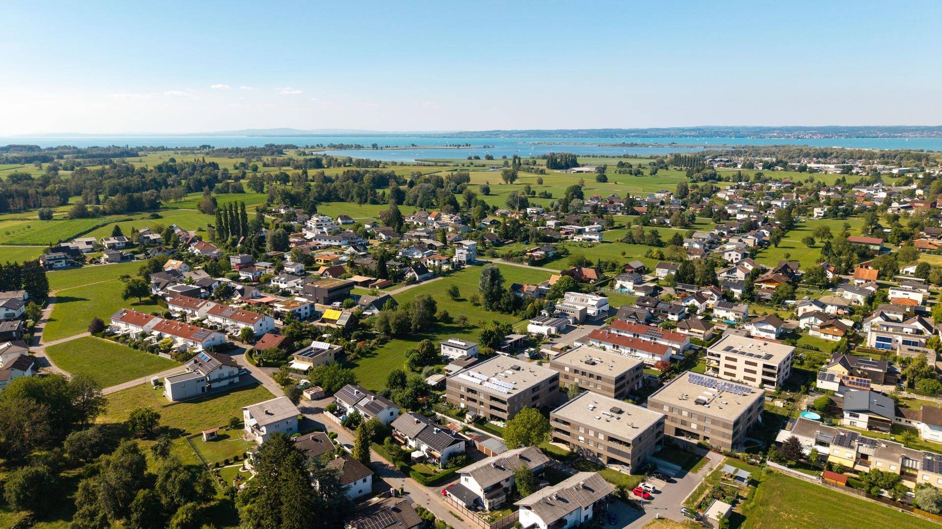 Weitläufige Luftaufnahme eines Wohngebiets mit modernen Gebäuden, See und Bergen.