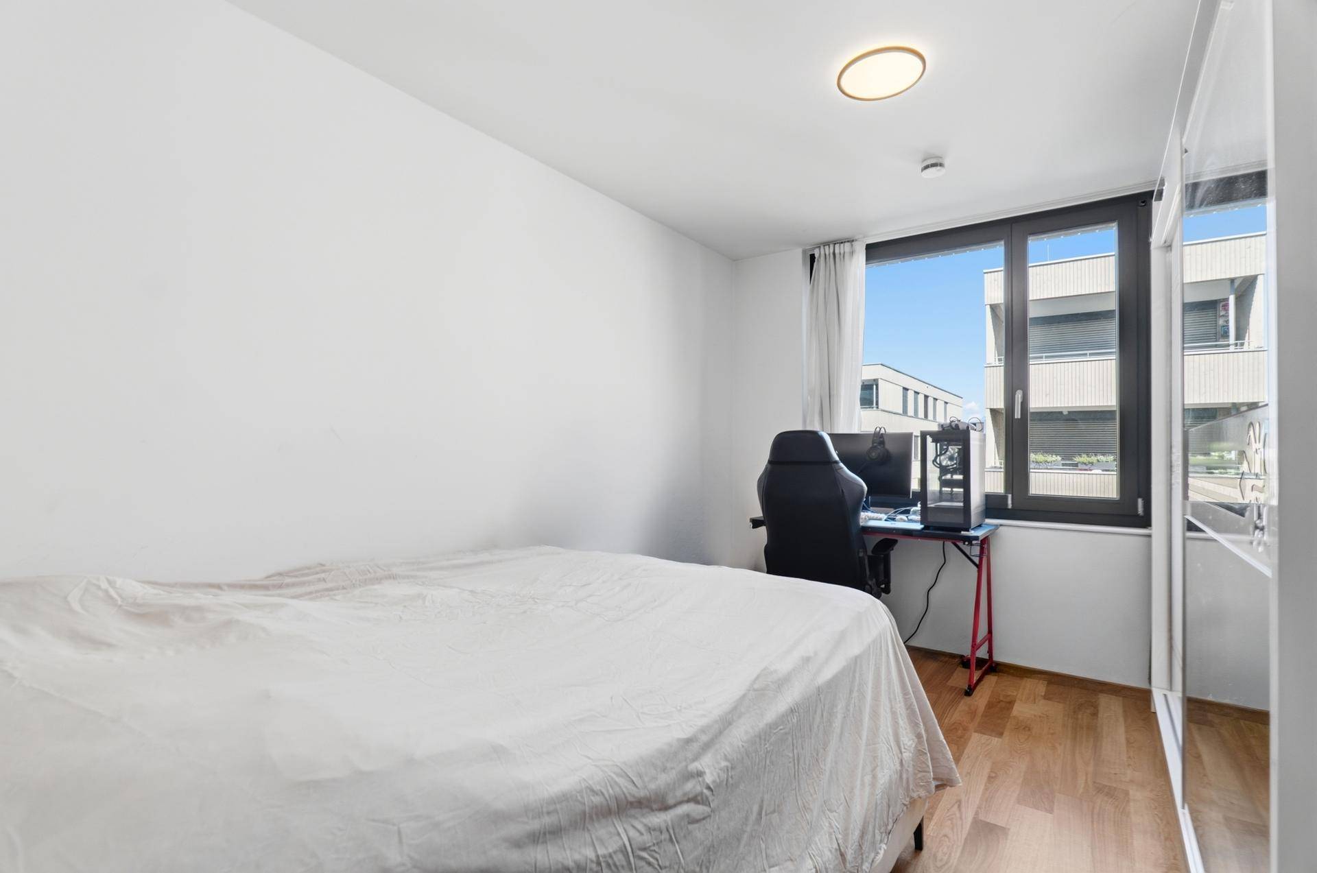 Helles Schlafzimmer mit Holzboden, großem Fenster und Blick ins Grüne.
