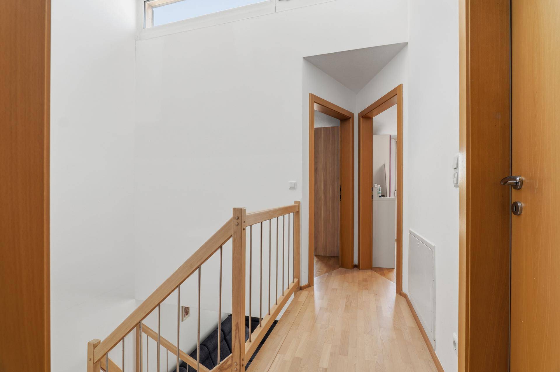 Heller Flur im Obergeschoss mit Holztreppe und mehreren Zimmertüren.